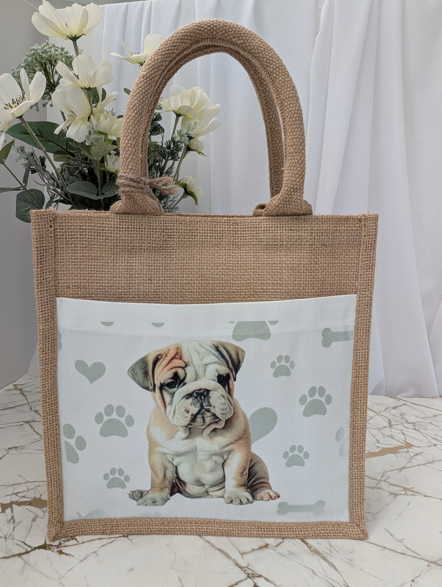 Bulldog tote bag made of sustainably sourced jute. It has a cream front pocket printed with cute bulldog image against a background of soft grey pawprints hearts and bones