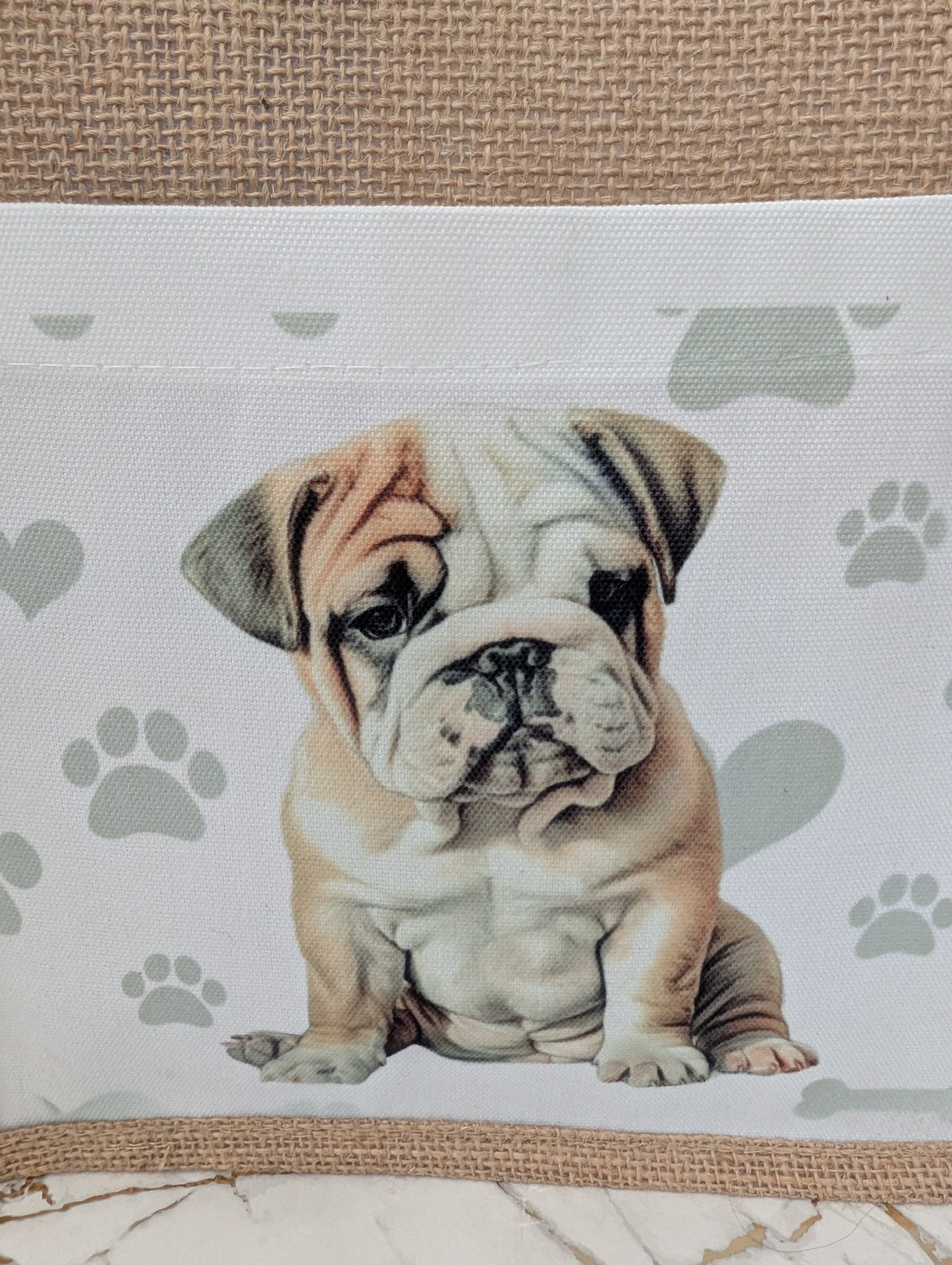 close up of Bulldog tote bag made of sustainably sourced jute. With cream front pocket printed with cute bulldog image against a background of soft grey pawprints hearts and bones