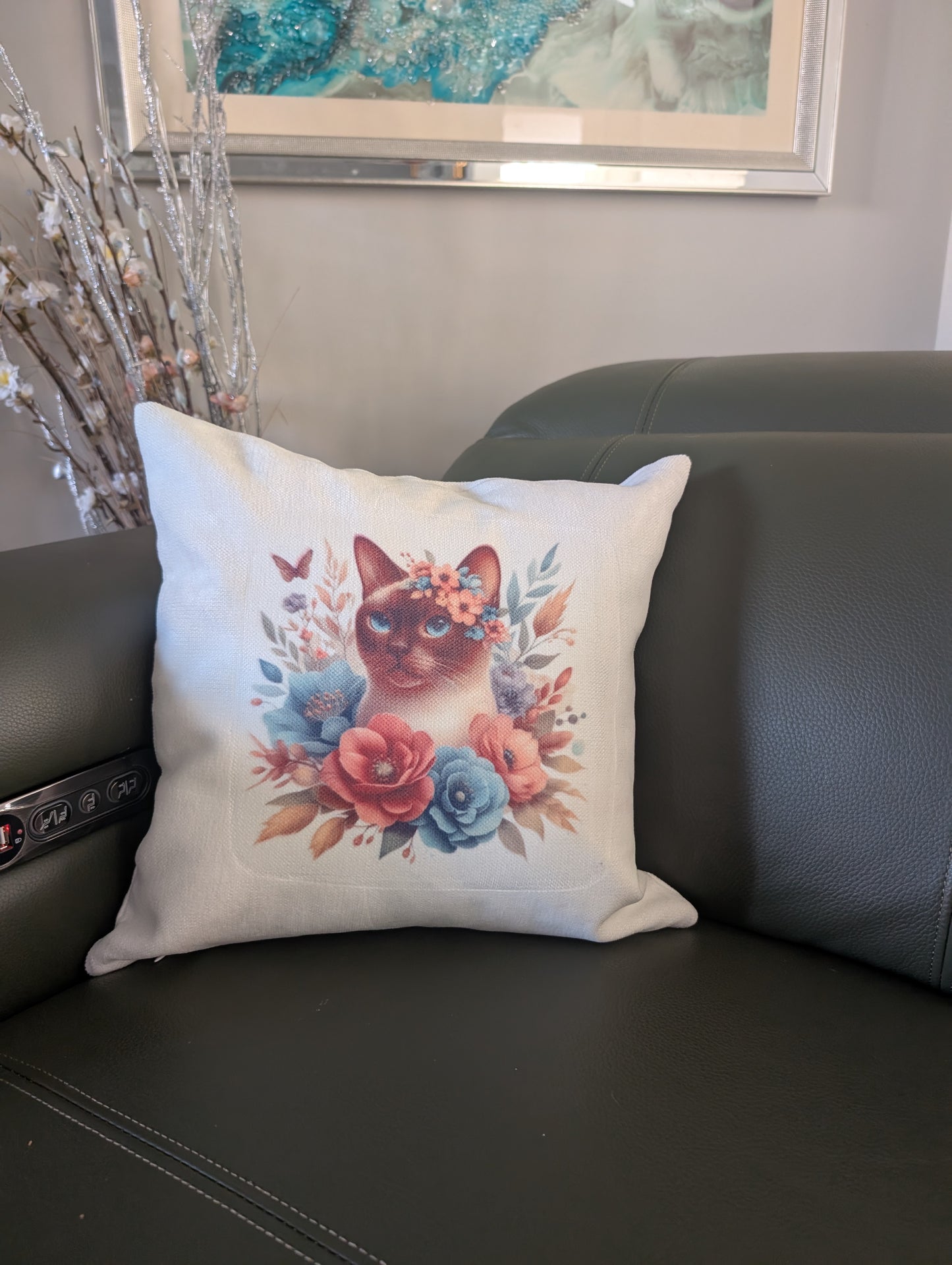 Decorative pillow with Siamese cat and floral design on a green leather couc