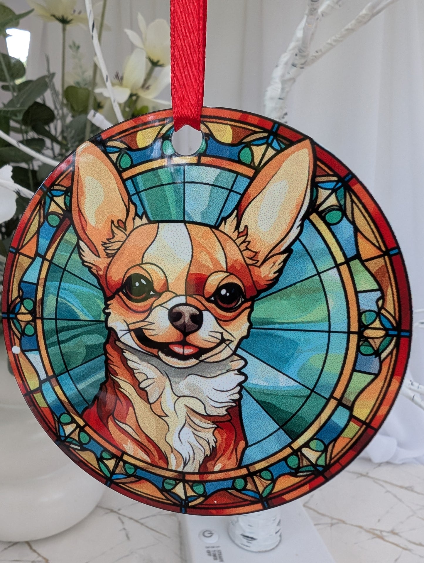 Close up of cute smiling chichuahua stained glass effect hanging ornament using blues yellows and browns. 9cm diameter hanging on a red ribbon