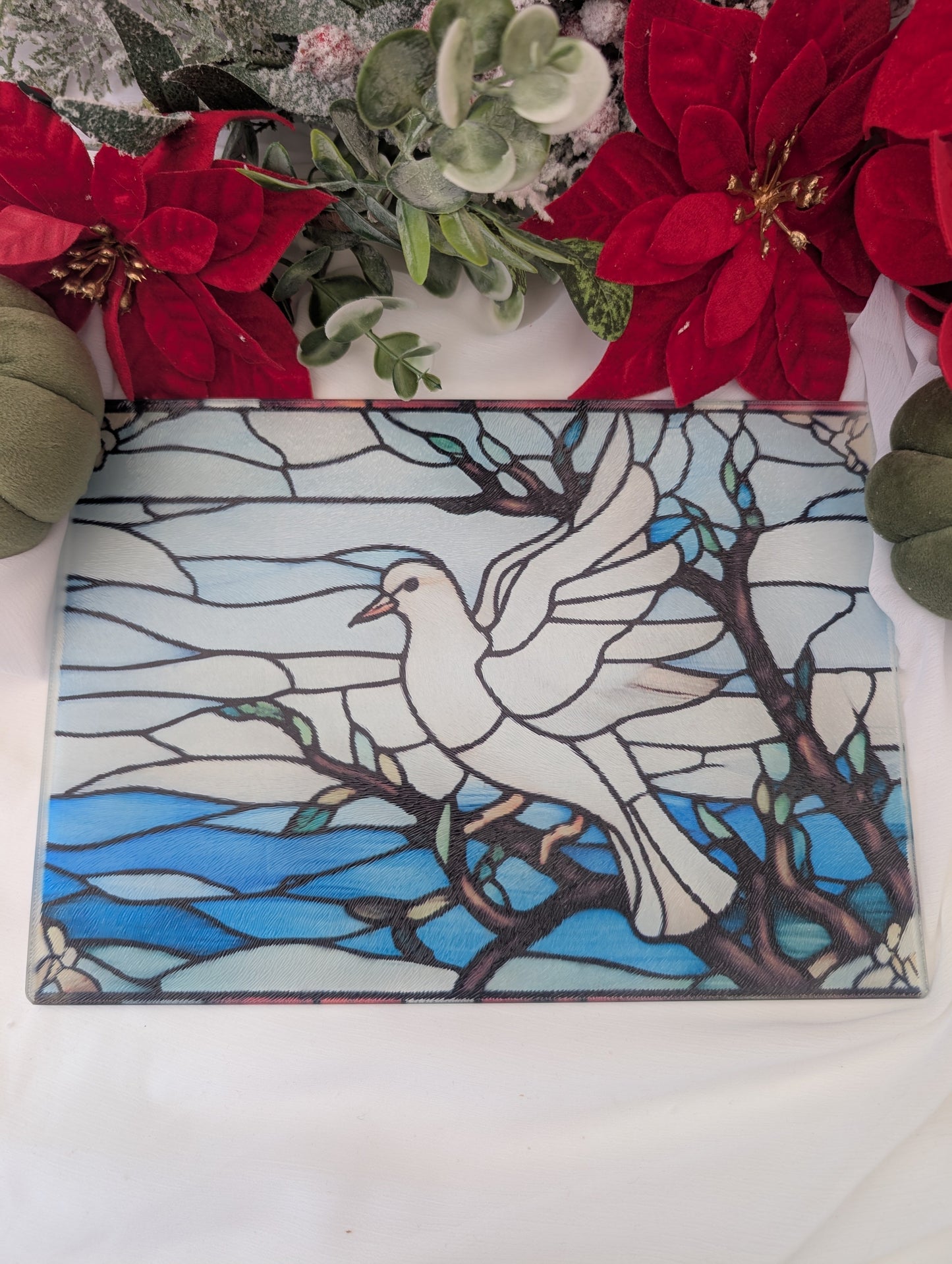 Decorative stained glass chopping board with a white dove design on a blue background, surrounded by red flowers and greenery.