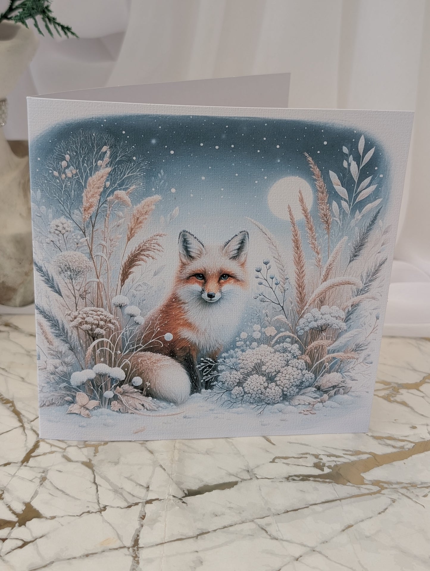 Greeting card with a fox illustration in a snowy landscape on a marble surface.