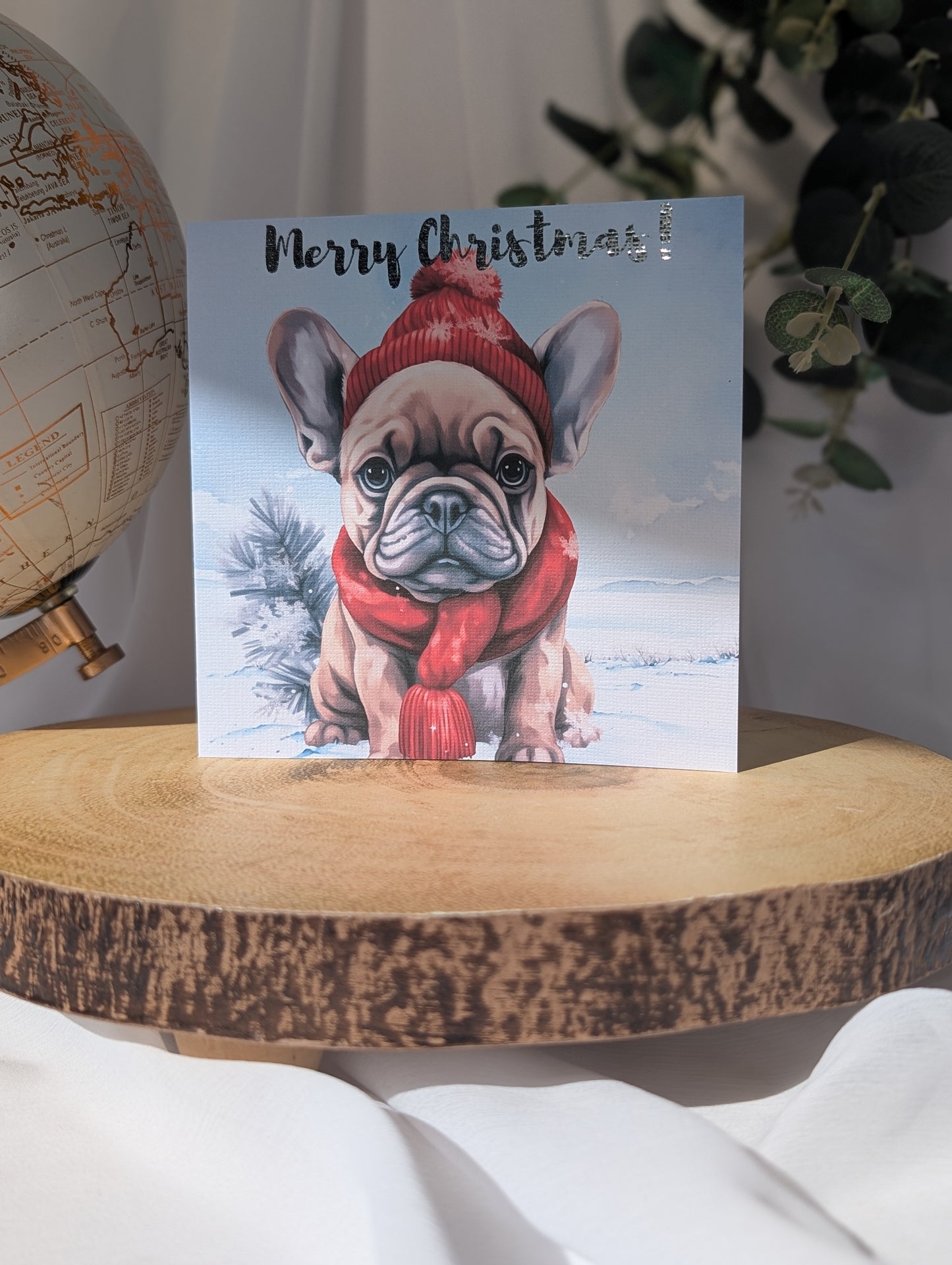 French Bulldog Christmas card with a dog wearing a hat and scarf on a wooden surface.