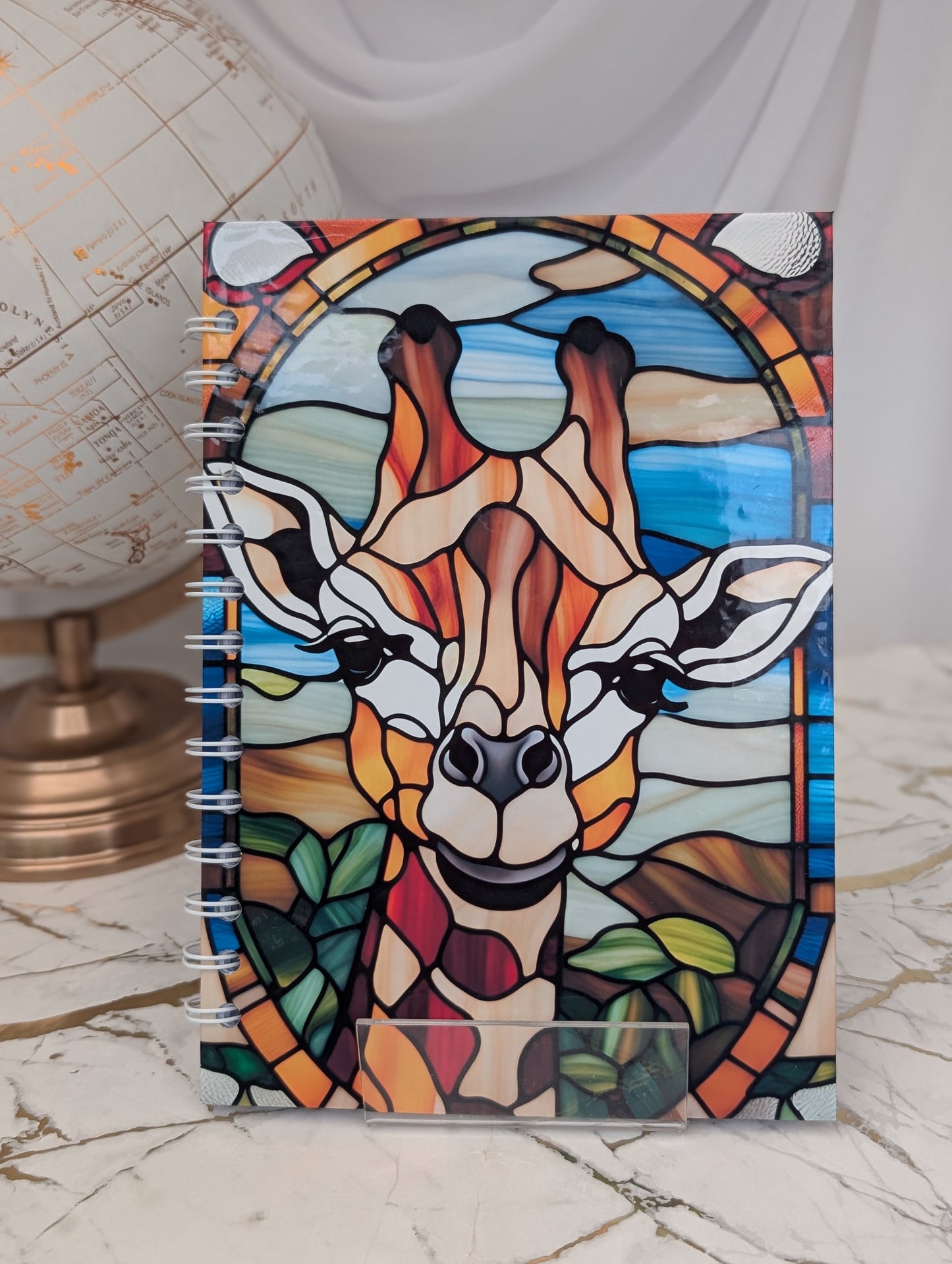 A spiral-bound notebook with a stained glass effect design featuring a giraffe's face on the cover.
