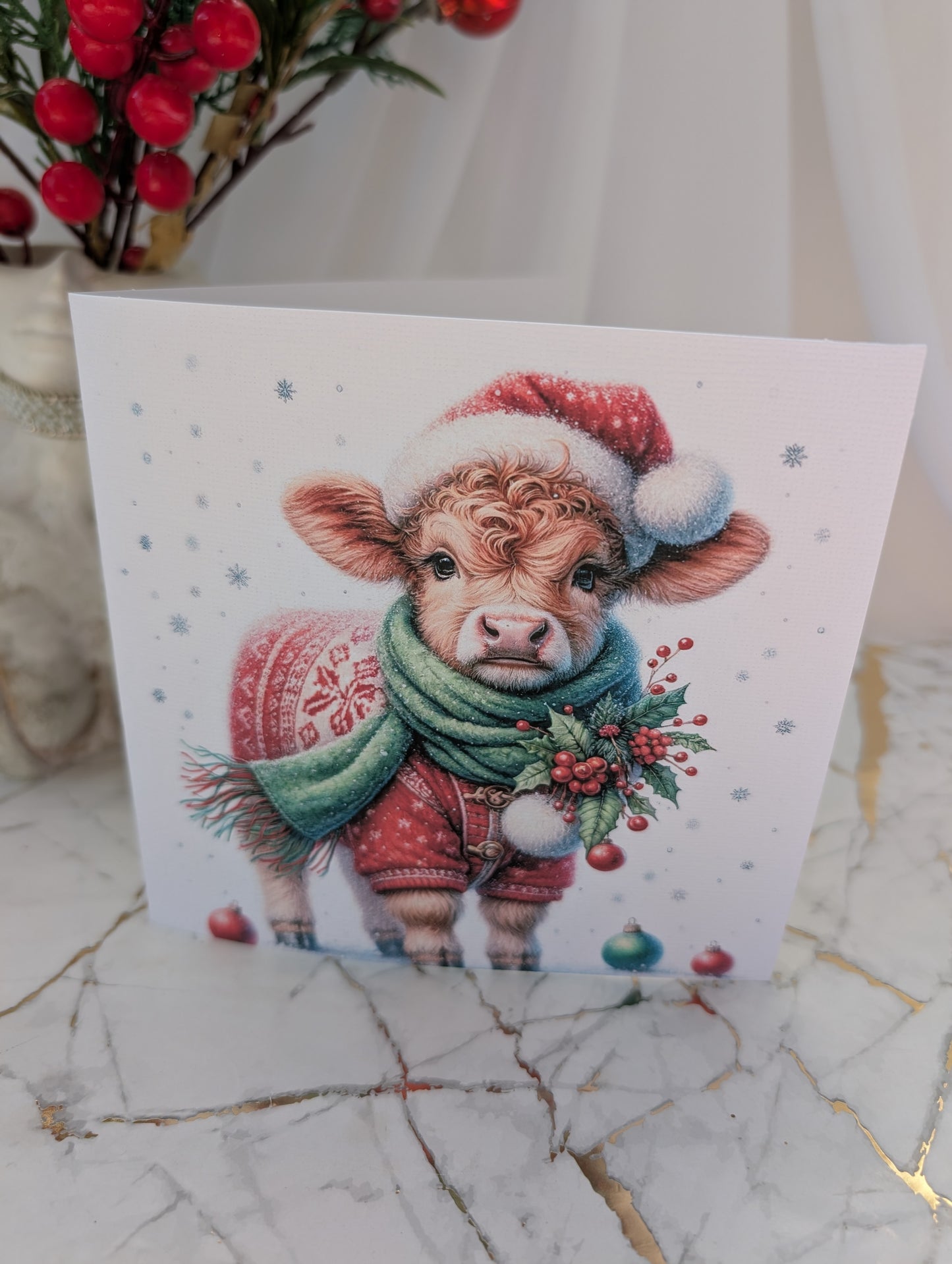 Card with a cow wearing a Santa hat and Christmas sweater on a marble surface.