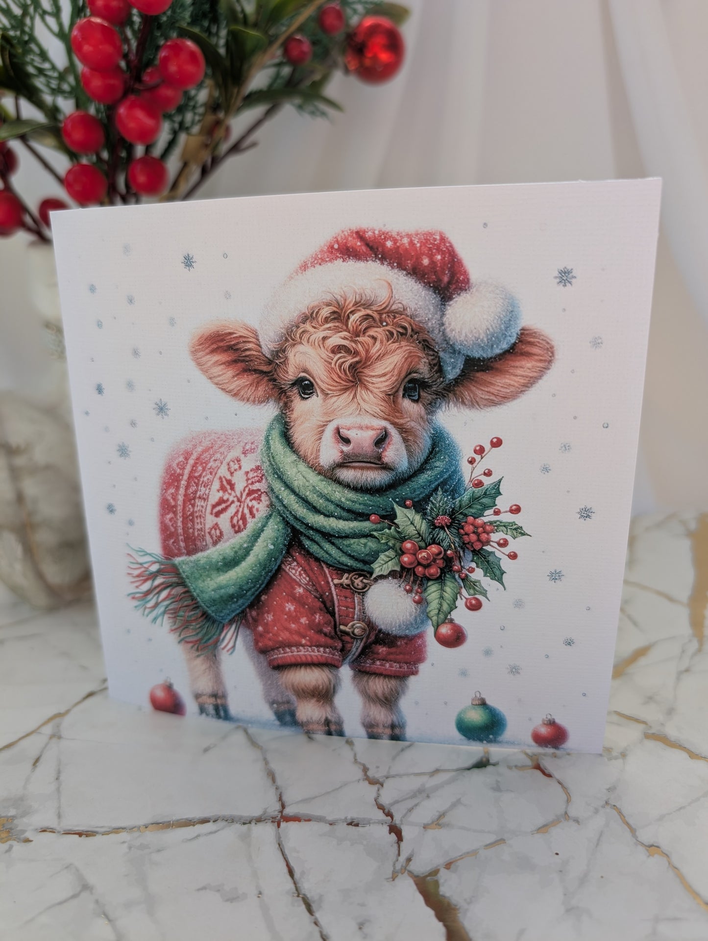 Highland cow Christmas card - cow wearing a Santa hat and scarf on a marble surface.