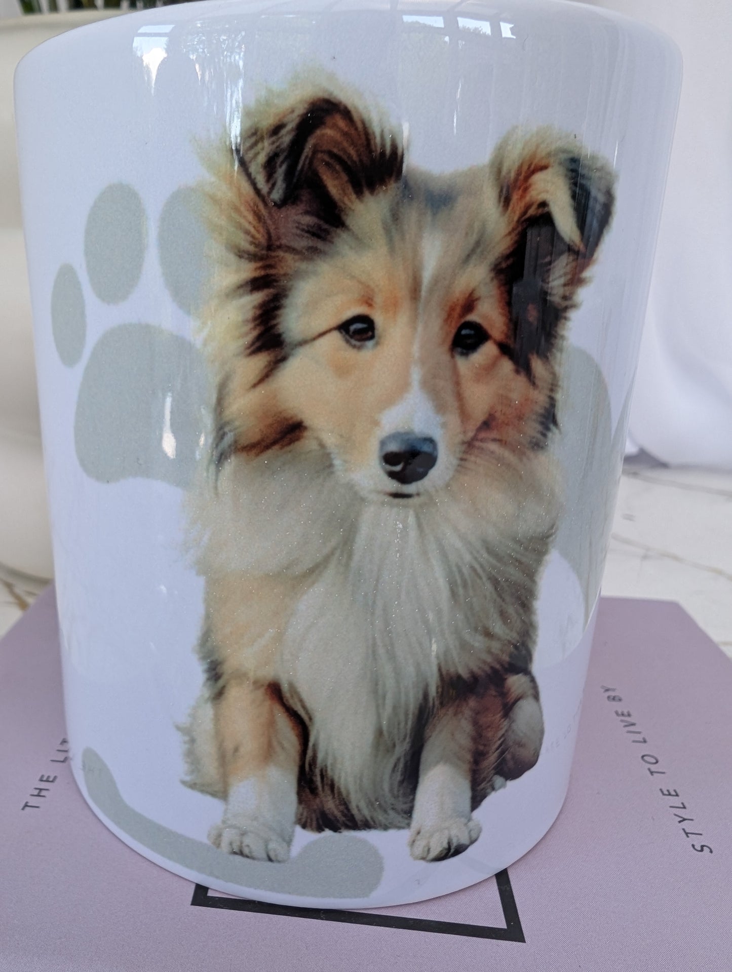 Close up of 11oz white ceramic Border Collie mug, with watercolour style image of Border collie against a background of soft grey hearts, pawprints and bones