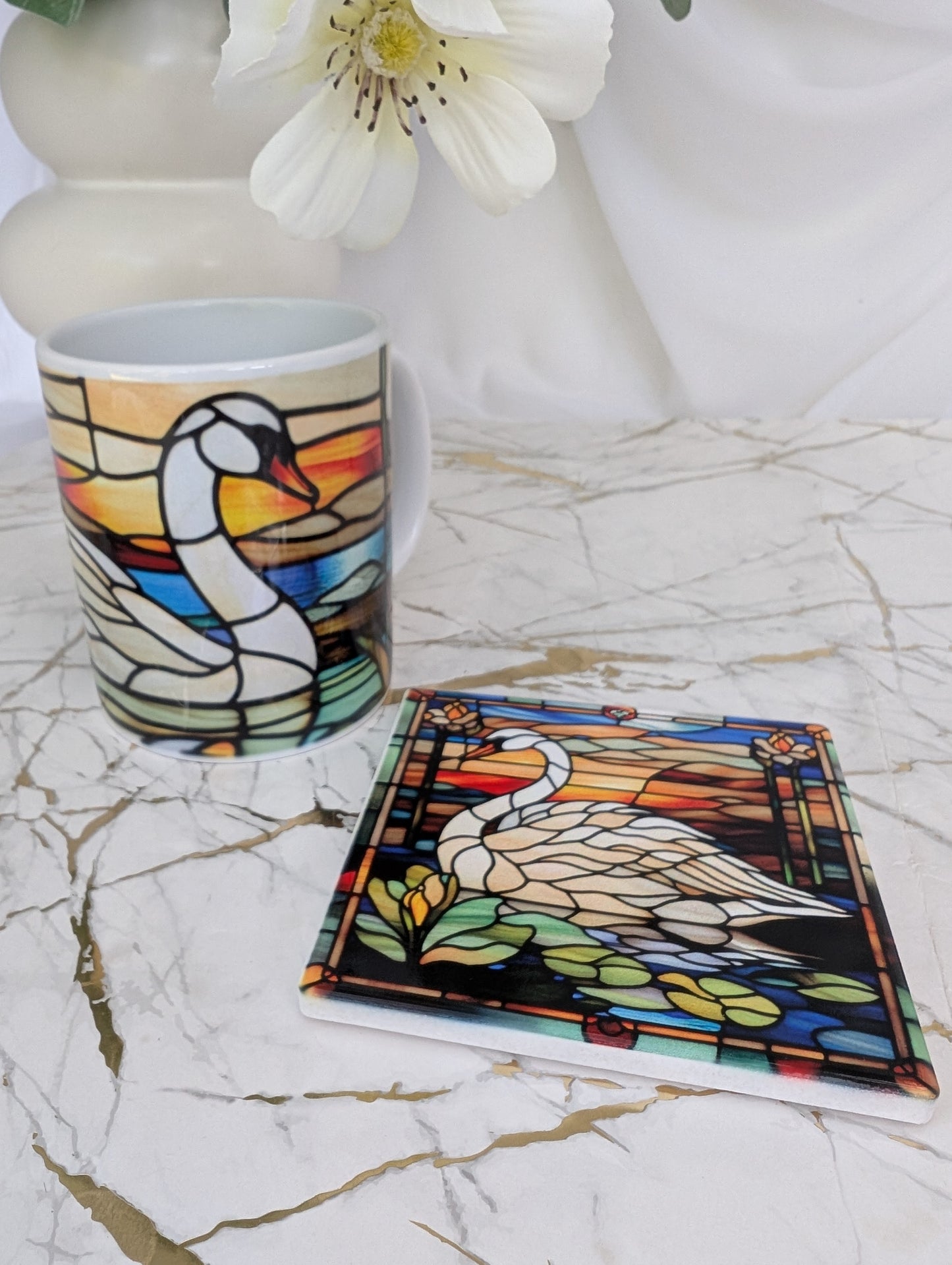 Top view of a square swan stained glass effect ceramic coaster on a marble surface with a stained glass ceramic mug