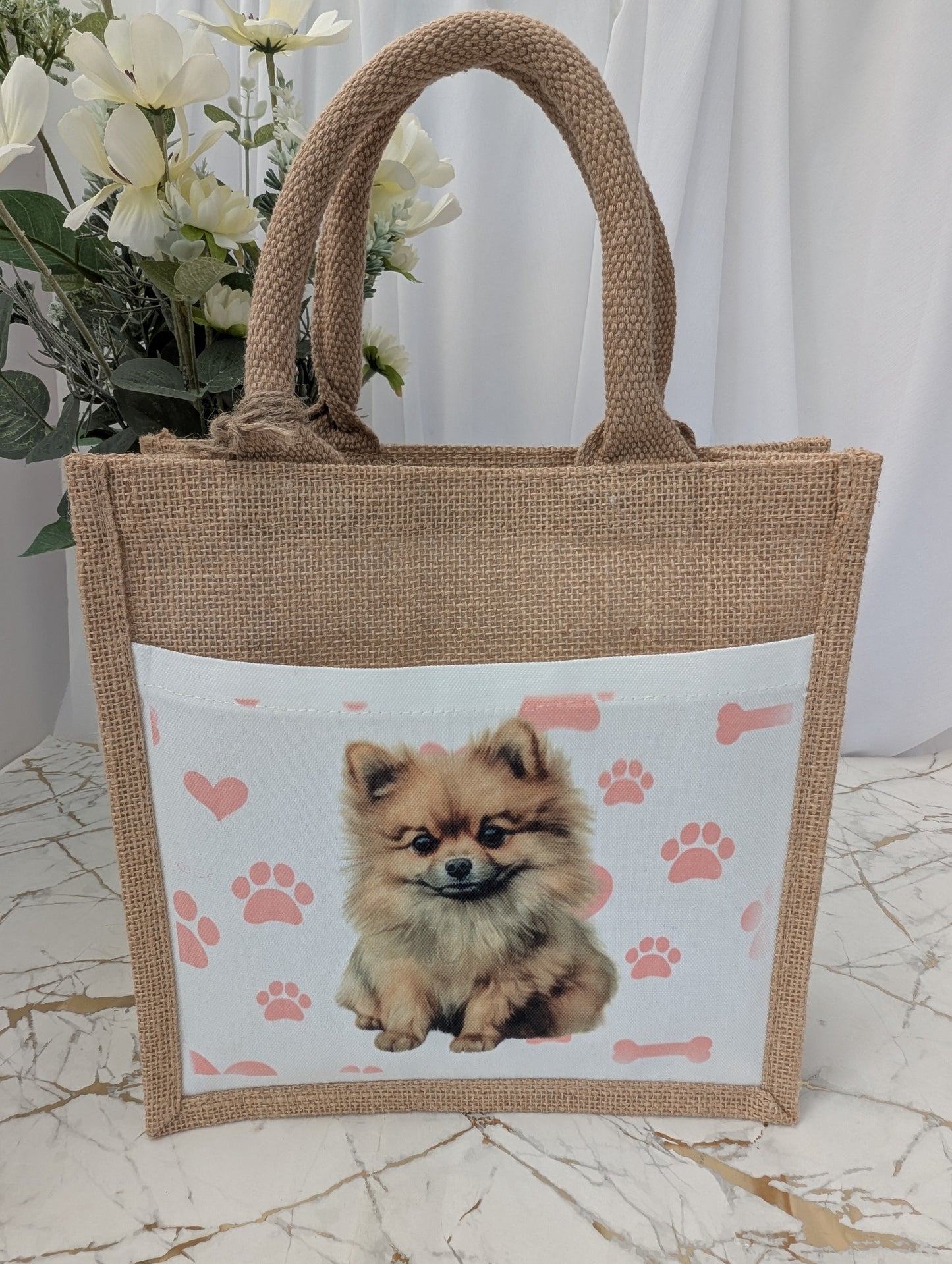 Eco friendly jute tote bag with cream front pocket printed with Pomeranian dog and background of pink pawprint, hearts and bones