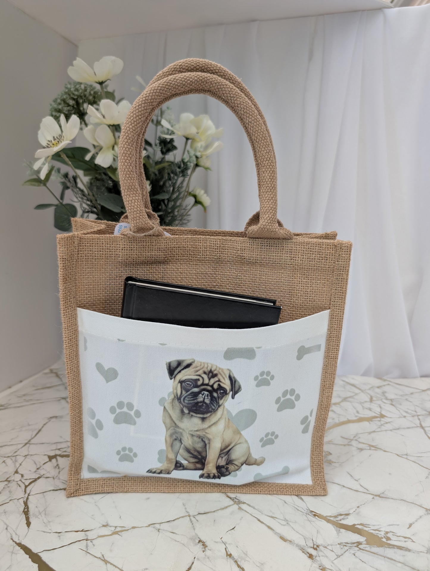 Eco friendly jute tote bag showing book inside front pocket, printed with pug against paw, heart and bone background