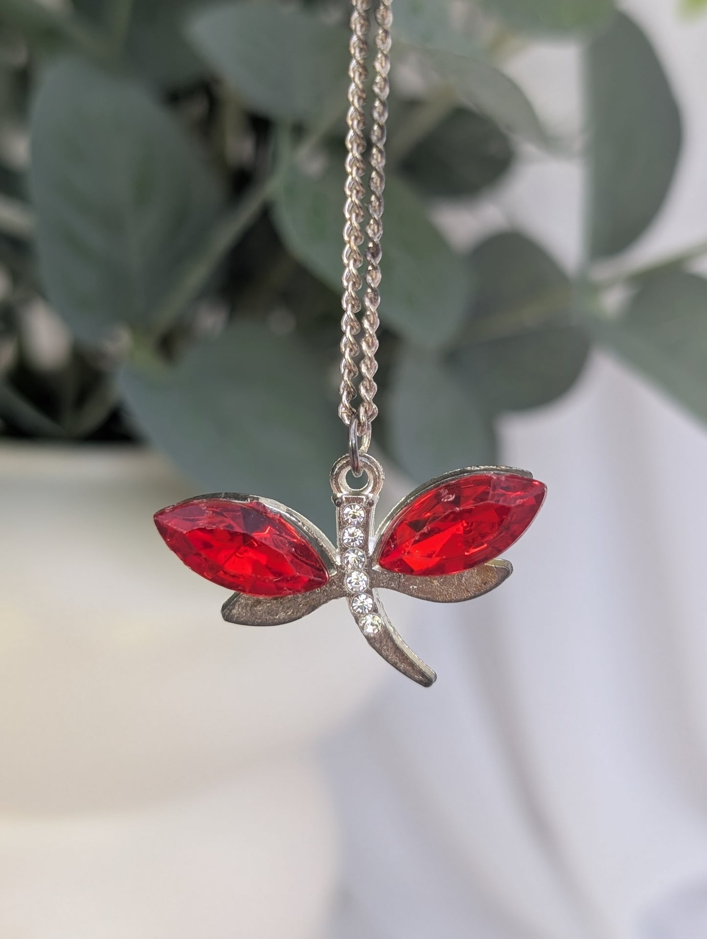mid distance shot of red crystal stone and silver tone dragonfly pendant against blurred green leaf background