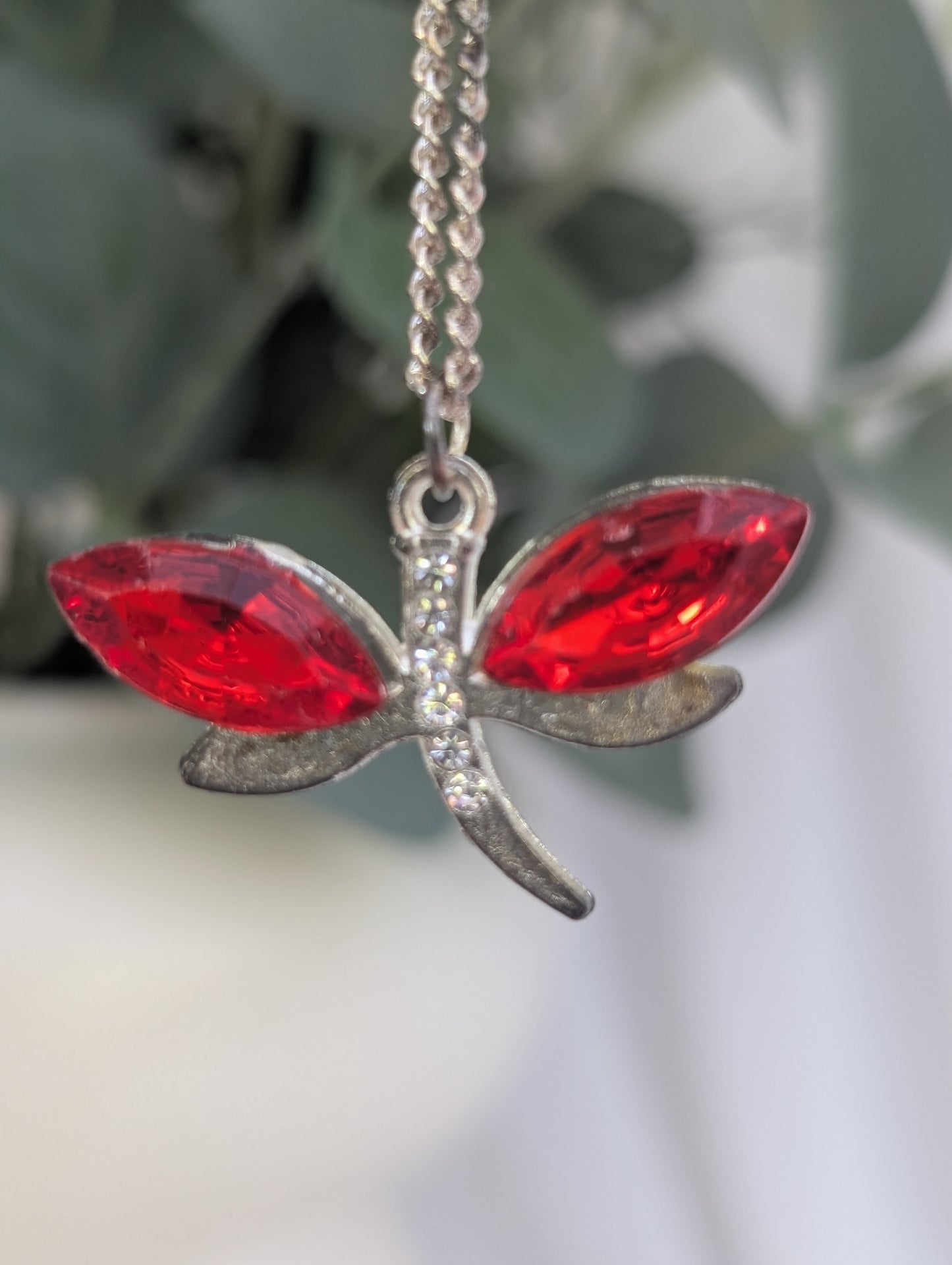 Close up of silver tone dragonfly pendant with red crystal and clear diamante stone accents
