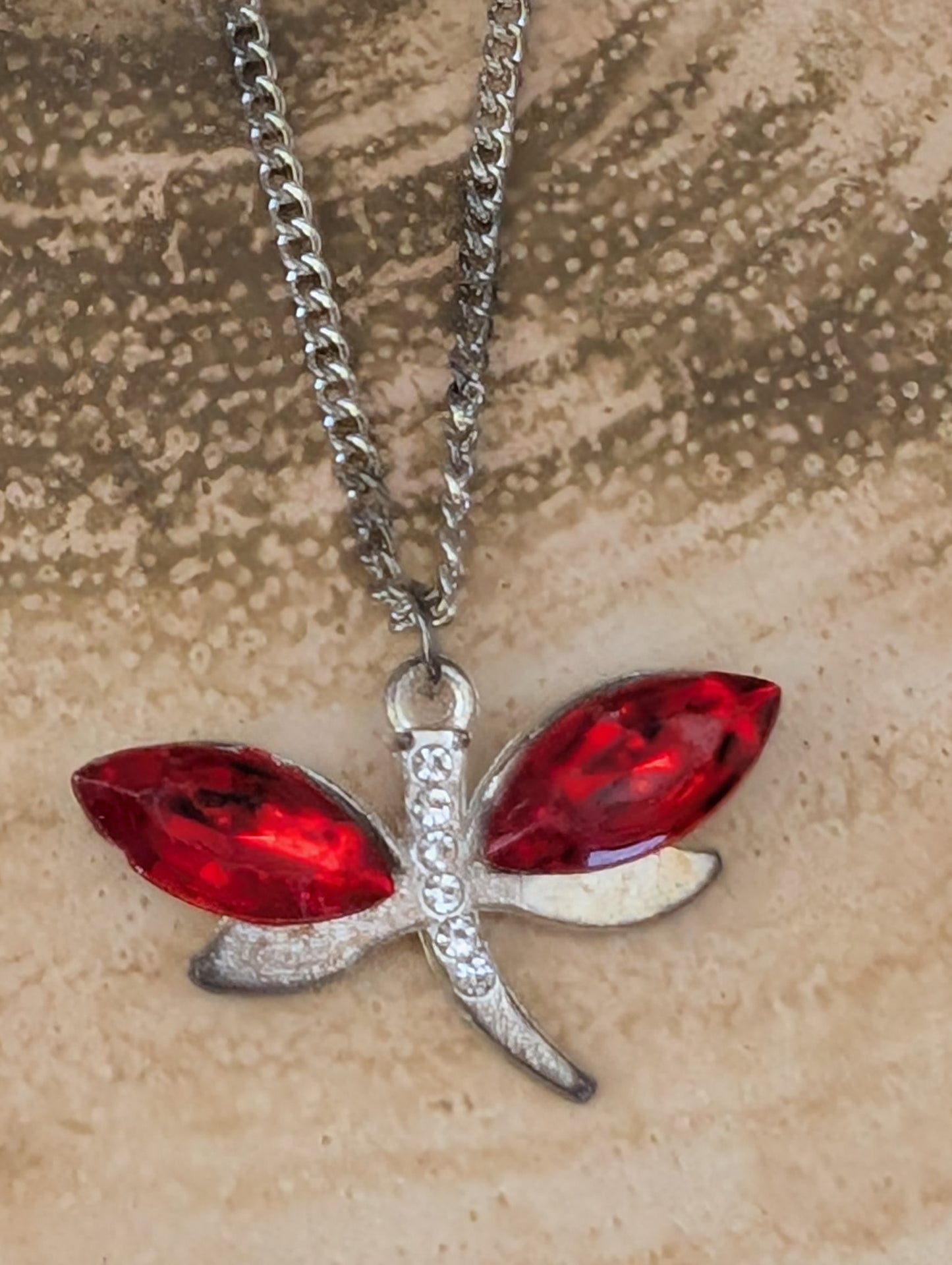 silver tone and red crystal stone pendant with clear diamante accent against a wooden background