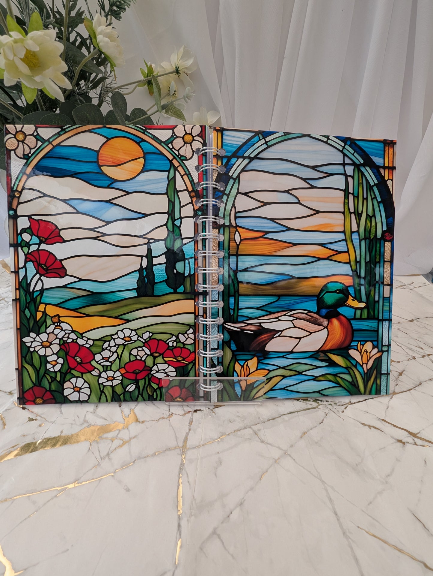 Front and back views of an A5 size handmade duck-themed, faux stained glass glossy notebook. Spiral bound, open to show front and back cover