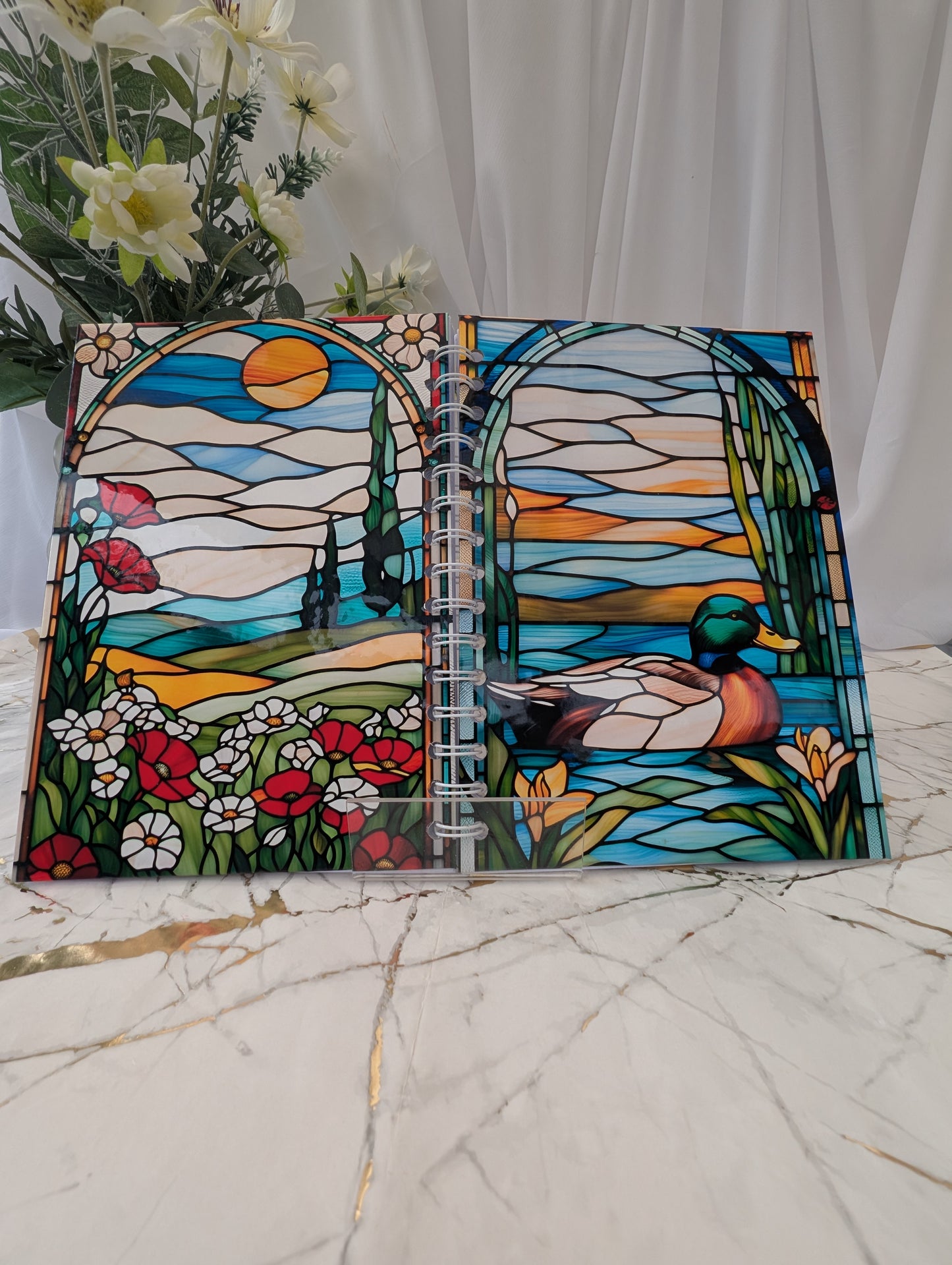 Front and back view of a handmade spiral bound, duck-themed, stained glass glossy notebook. Open to show front and back