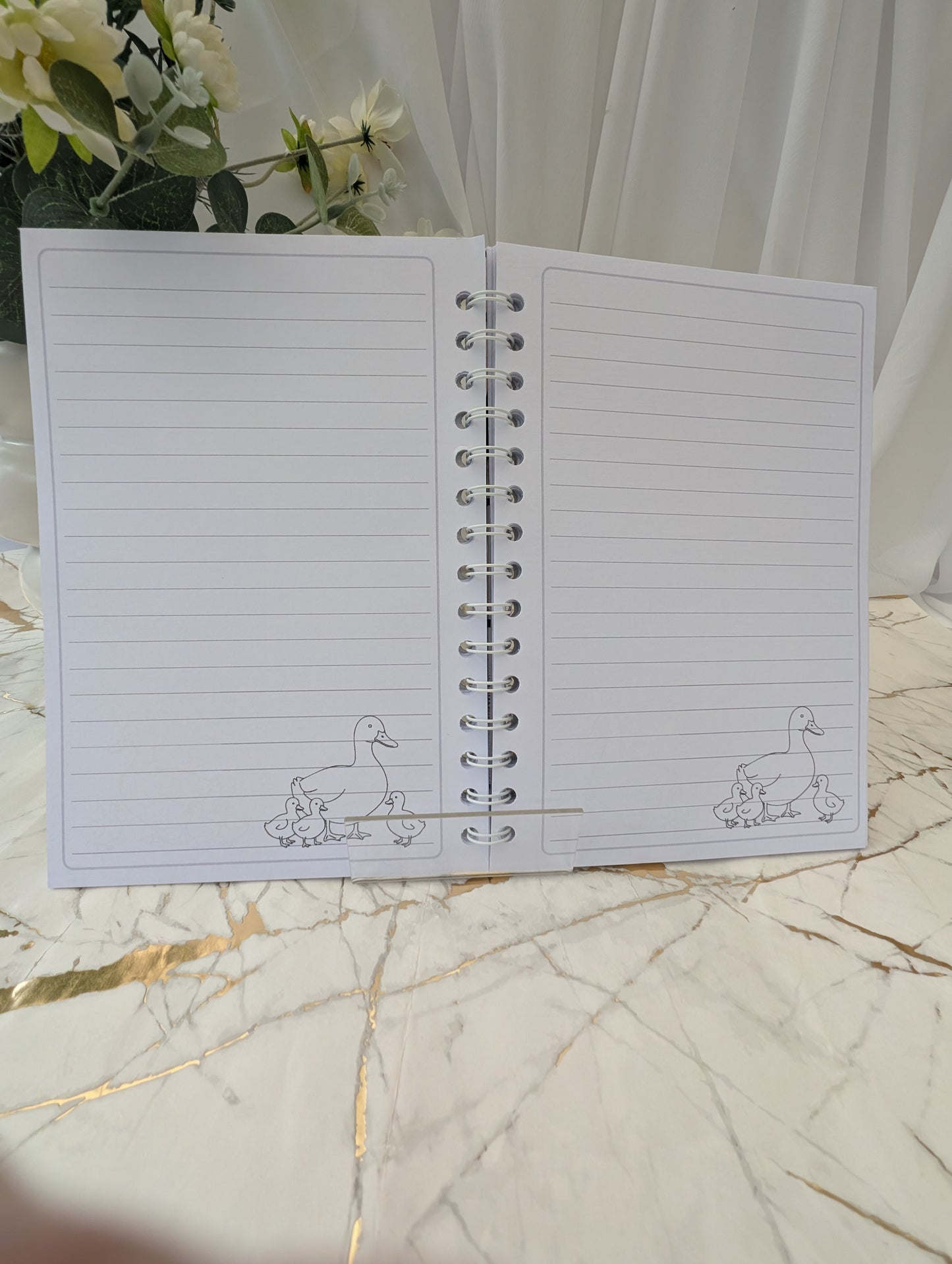 Open view of the inside pages of a duck, faux stained-glass style glossy notebook, 120gsm luxury paper hand printed with duck line drawing in the right hand colour.
