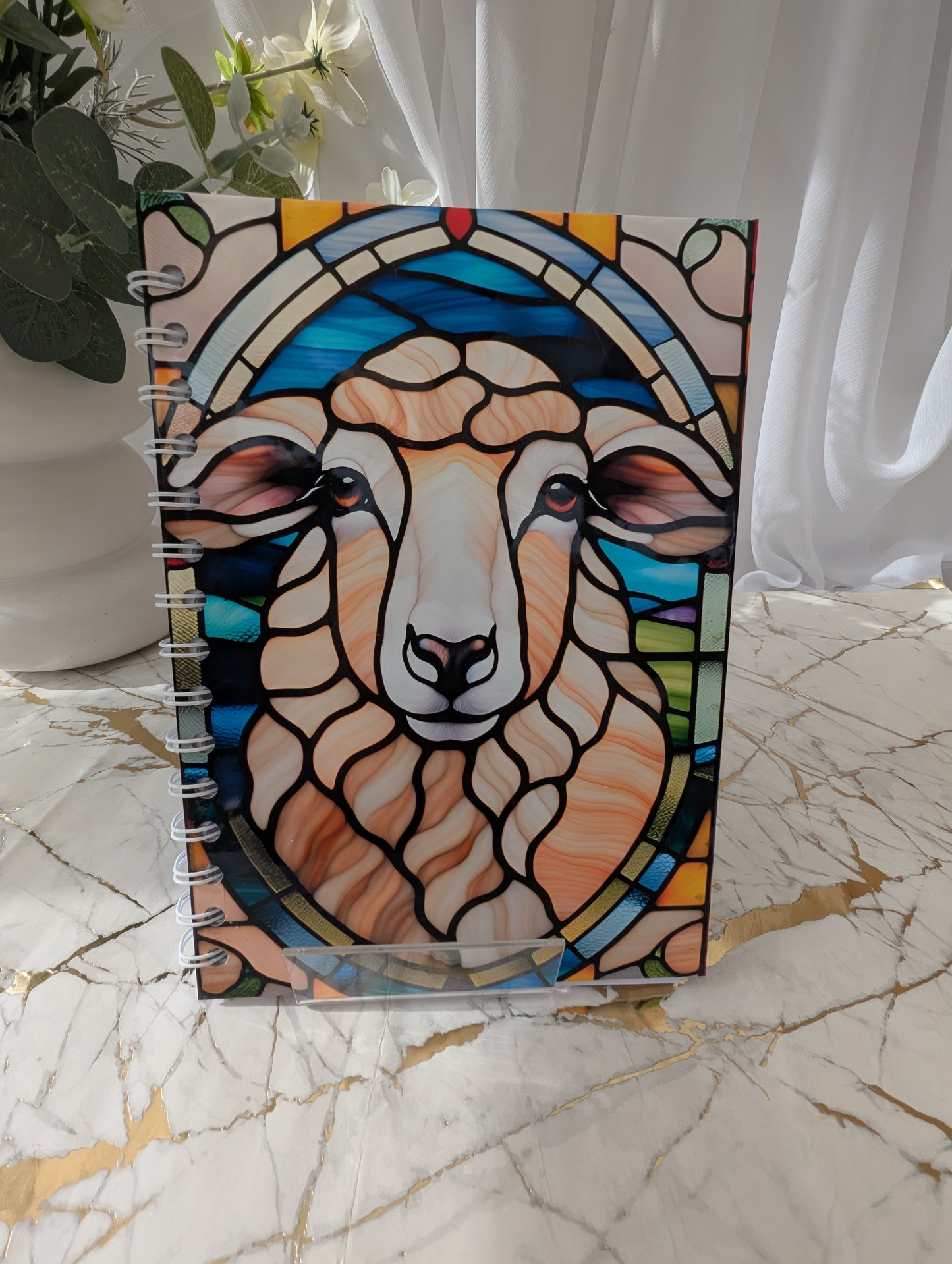 Close-up of A5 handmade spiral bound notebook with glossy cover, featuring a colourful faux stained glass sheep design.