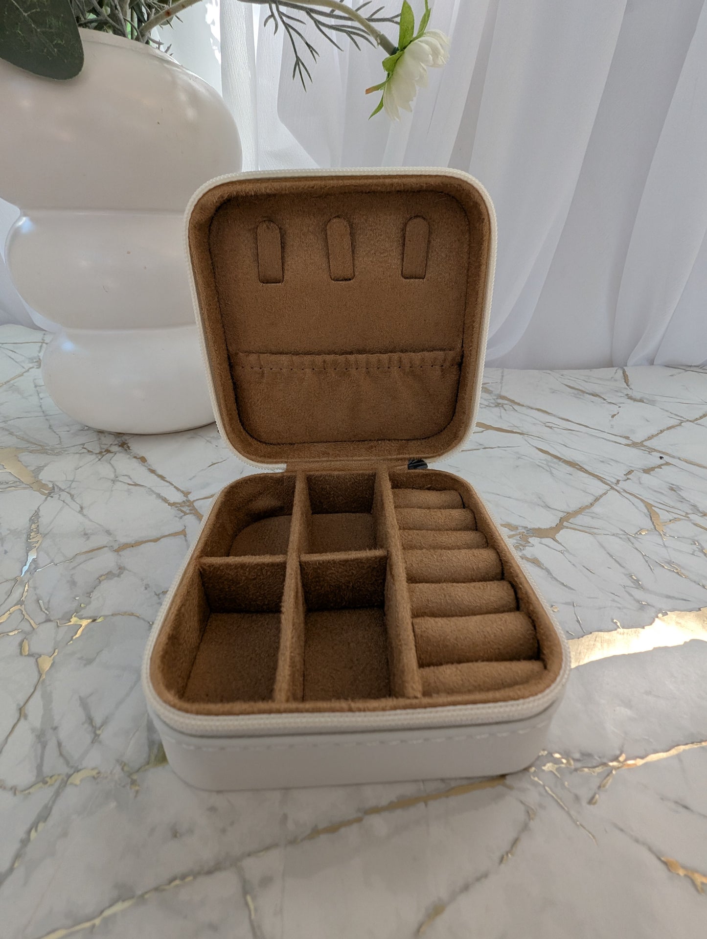 Open beige jewelry box with compartments on a marble surface