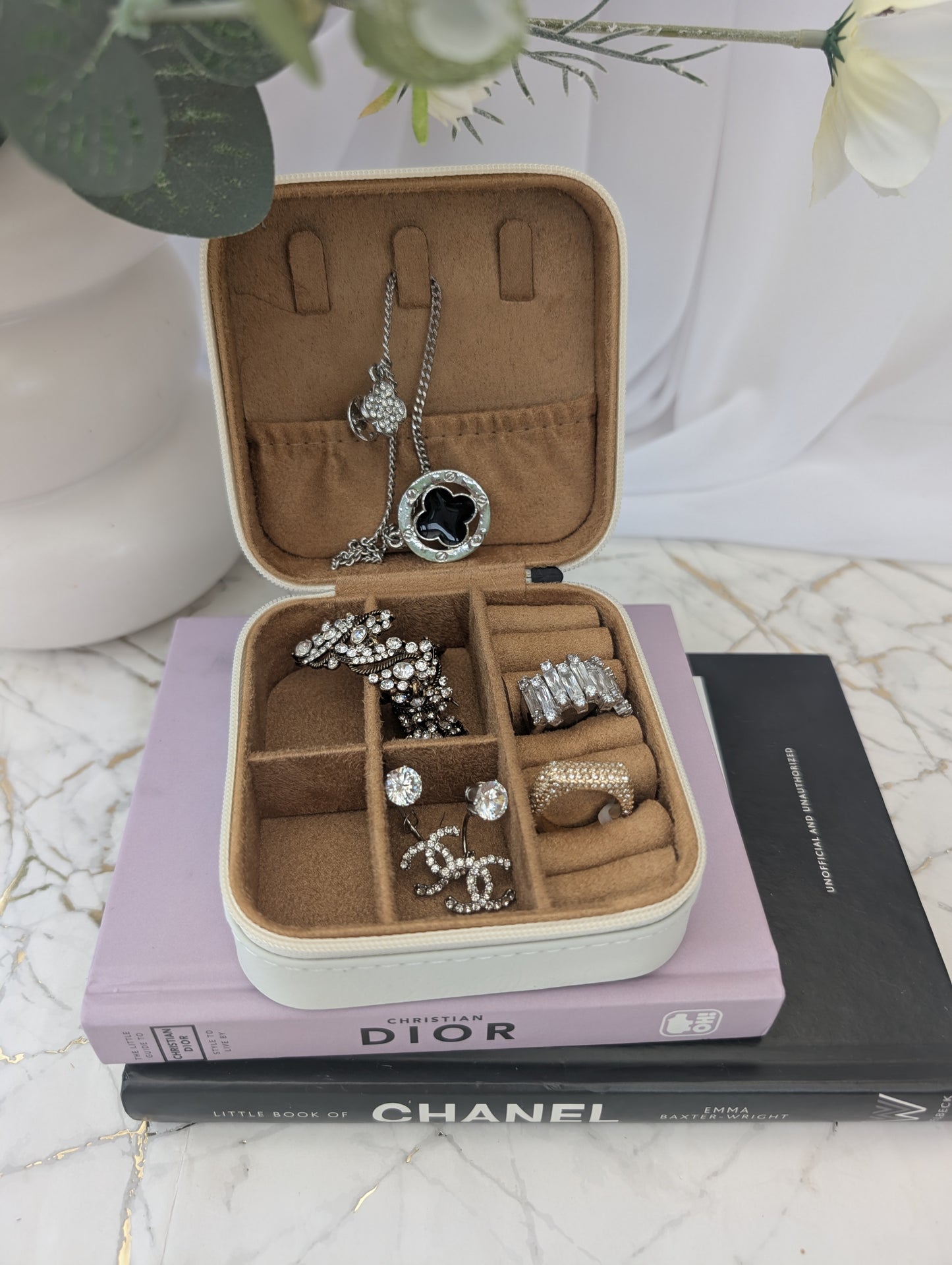 Open travel jewelry box with rings on top of Dior and Chanel books