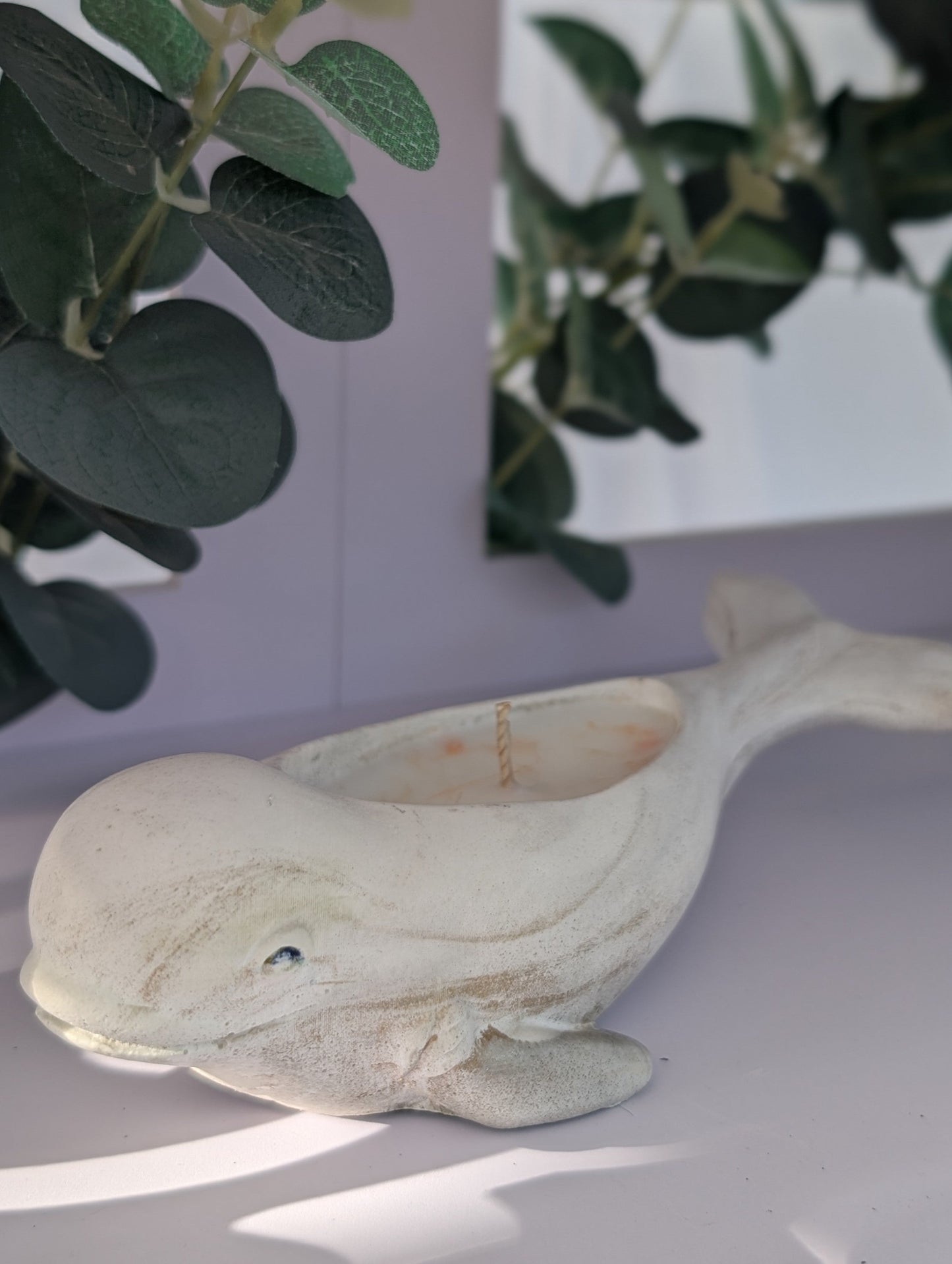 Decorative dolphin ornament on a white surface with green leaves in the background