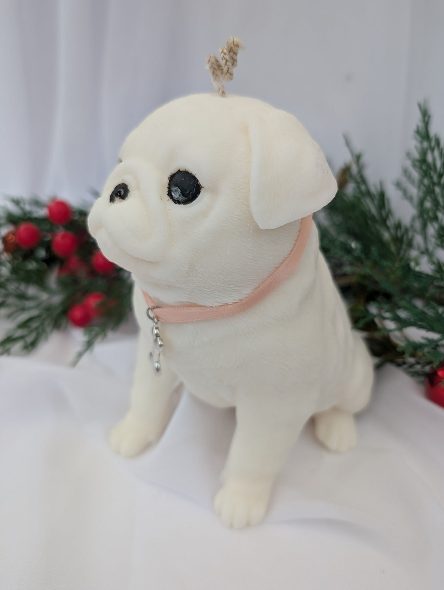 Left side view of white coconut and rapeseed wax moulded Pug Dog candle with ribbon and silver tone bone charm