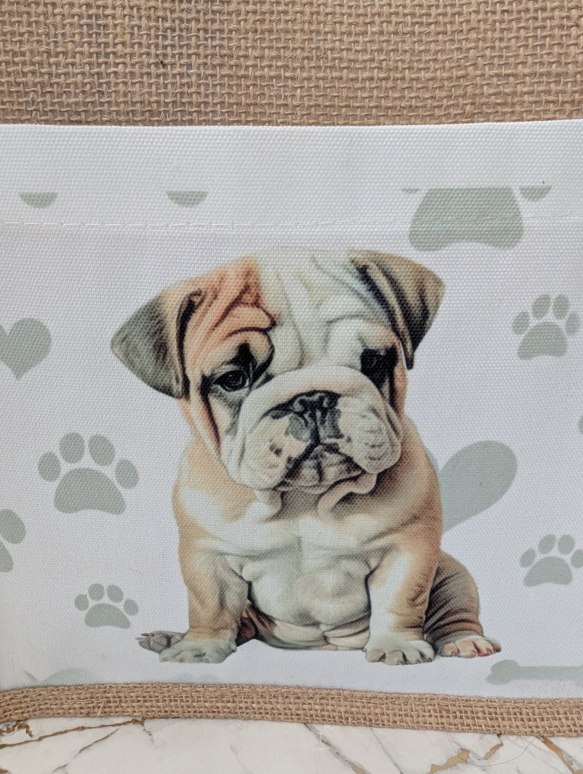 close up of Bulldog tote bag made of sustainably sourced jute.  With cream front pocket printed with cute bulldog image against a background of soft grey pawprints hearts and bones