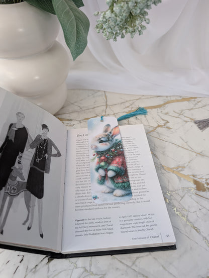 Open book with a decorative bookmark on a marble surface, next to a vase and plants.