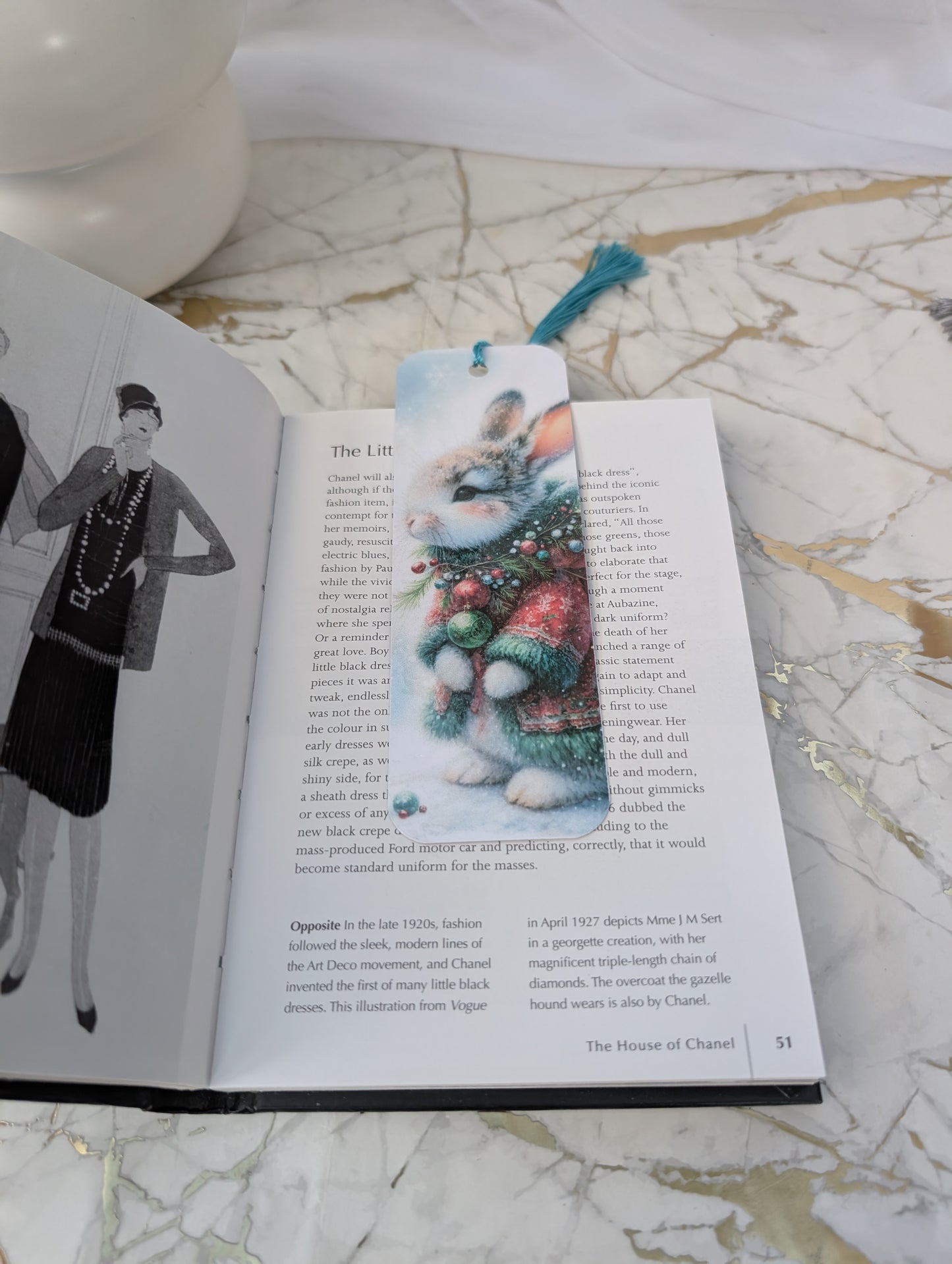 Book with a bookmark featuring a rabbit holding a bouquet, on a marble surface.