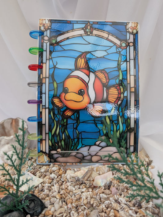 Refillable Discbound Stained glass clownfish notebook in an underwater scene with rocks and plants.