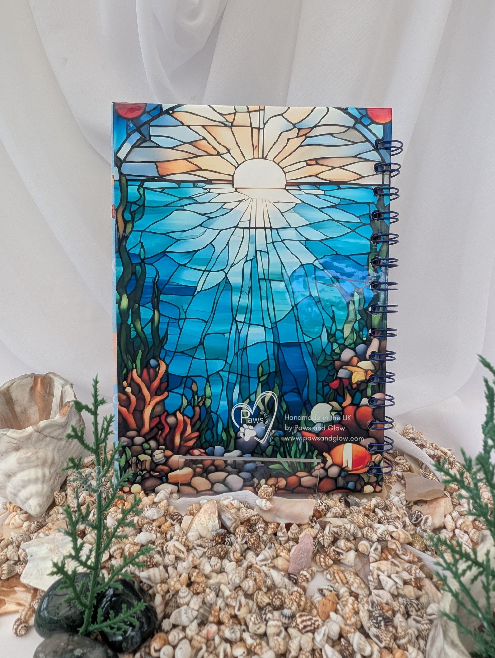 Decorative notebook with stained glass design of an underwater scene, surrounded by pebbles and small plants.