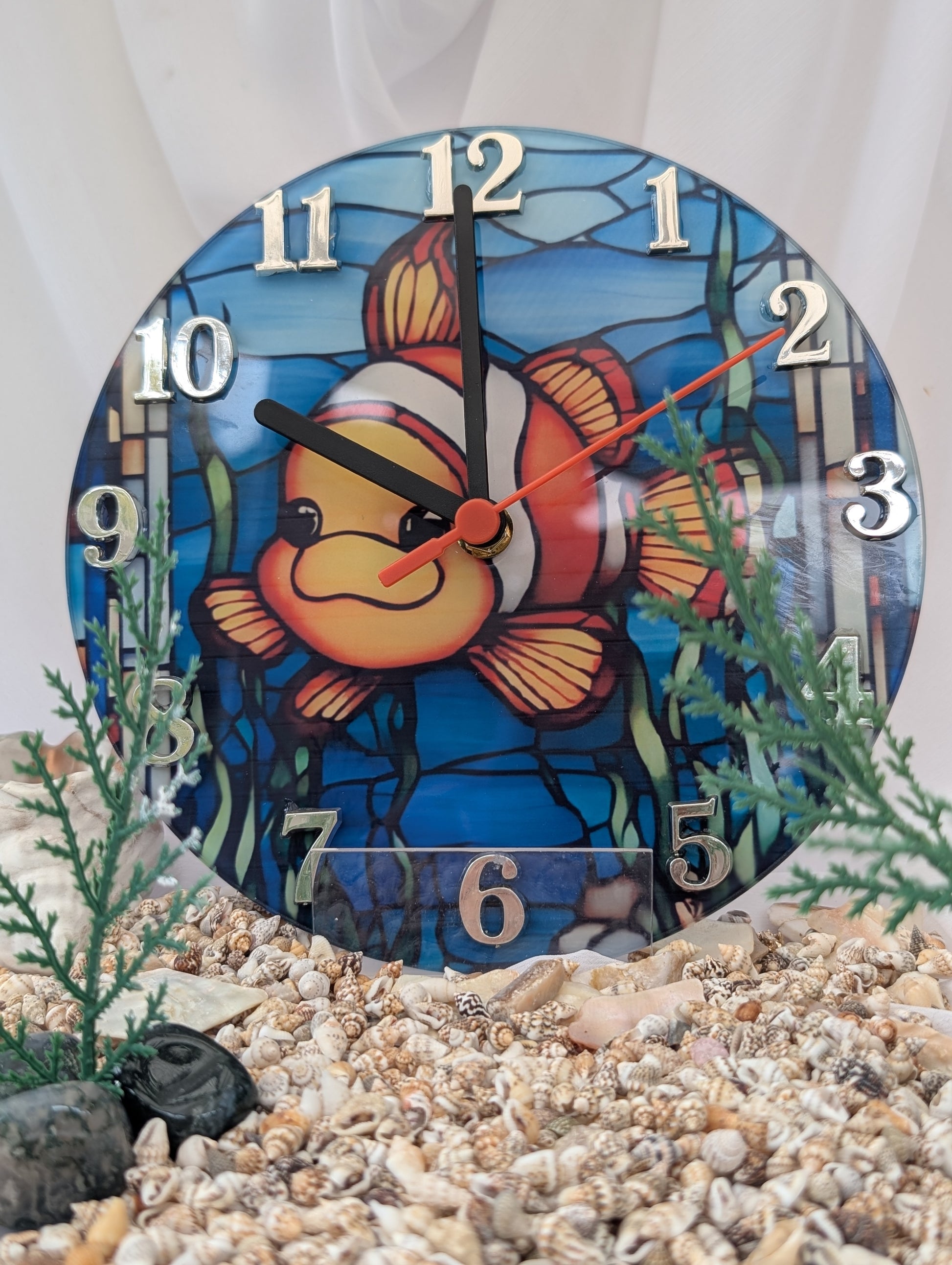 Decorative clock with a clownfish design on a pebbles and plants background
