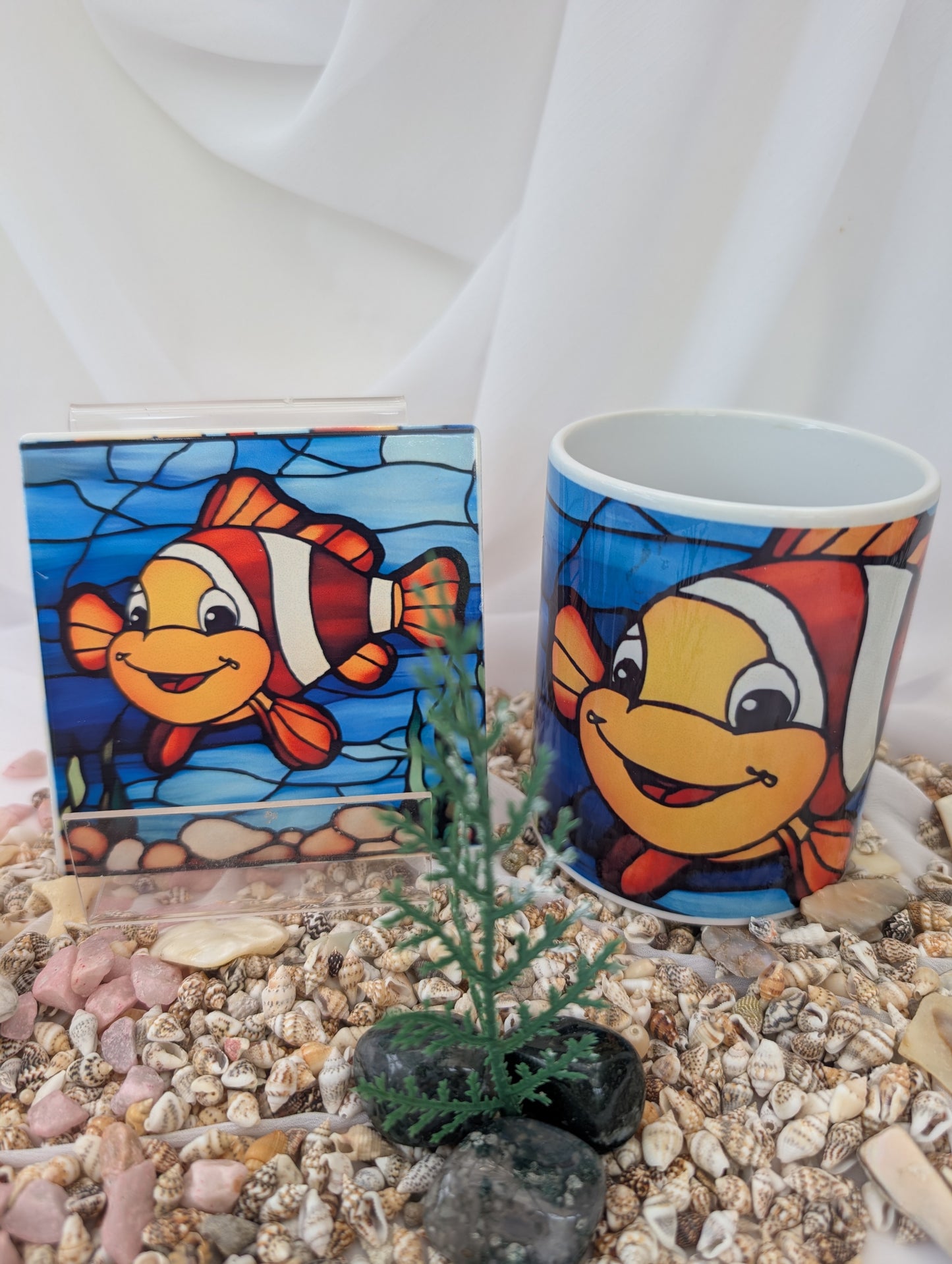 Cup with cartoon fish design and stained glass fish artwork on pebbles.