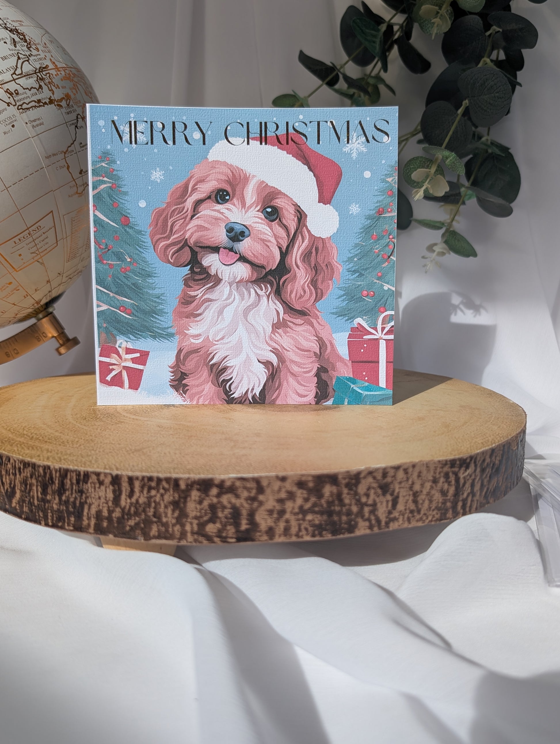 Dog Christmas card with a Cavapoo / Cockapoo wearing a Santa hat on a wooden surface.