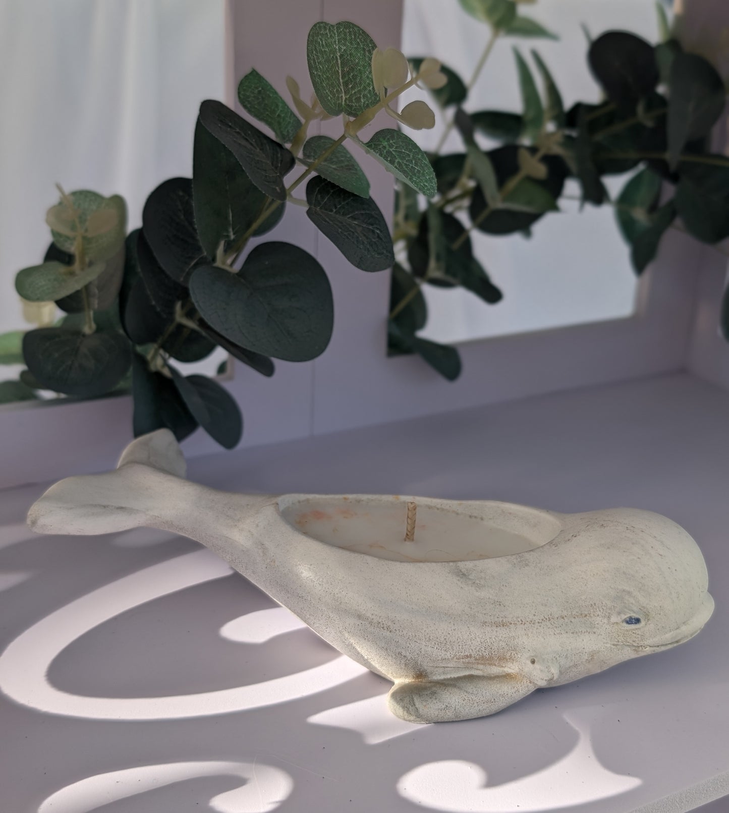 Decorative dolphin figurine on a surface with green foliage in the background