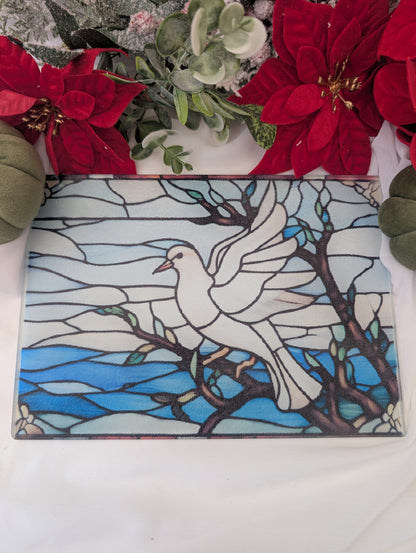 Decorative stained glass chopping board with a white dove design on a blue background, surrounded by red flowers and greenery.