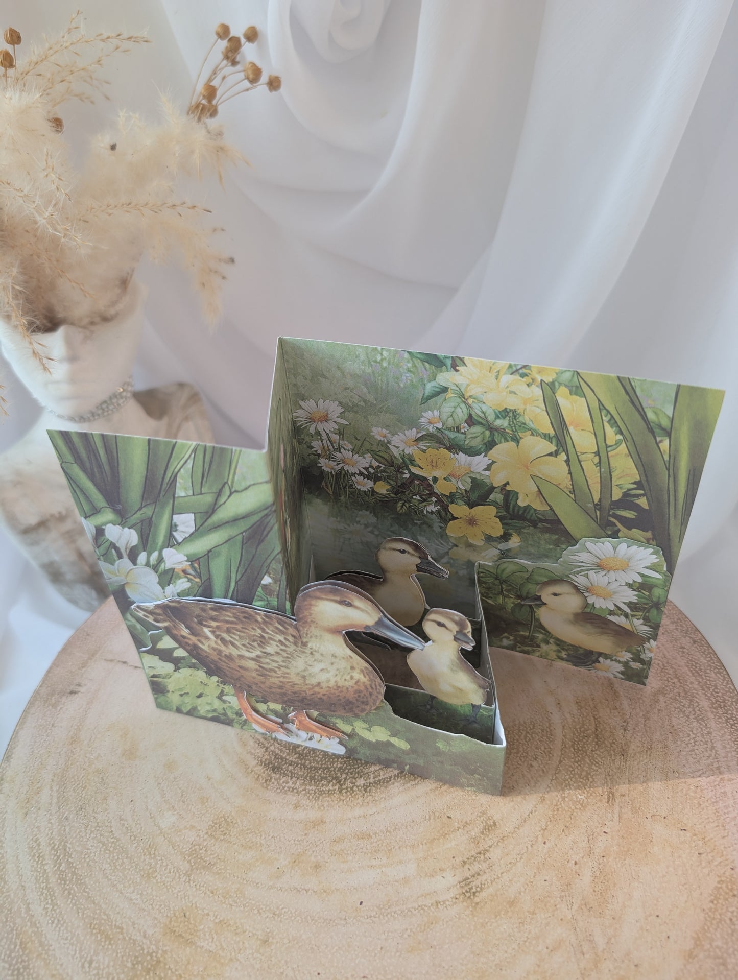 Pop up birthday card with  ducks and flowers on a wooden surface.