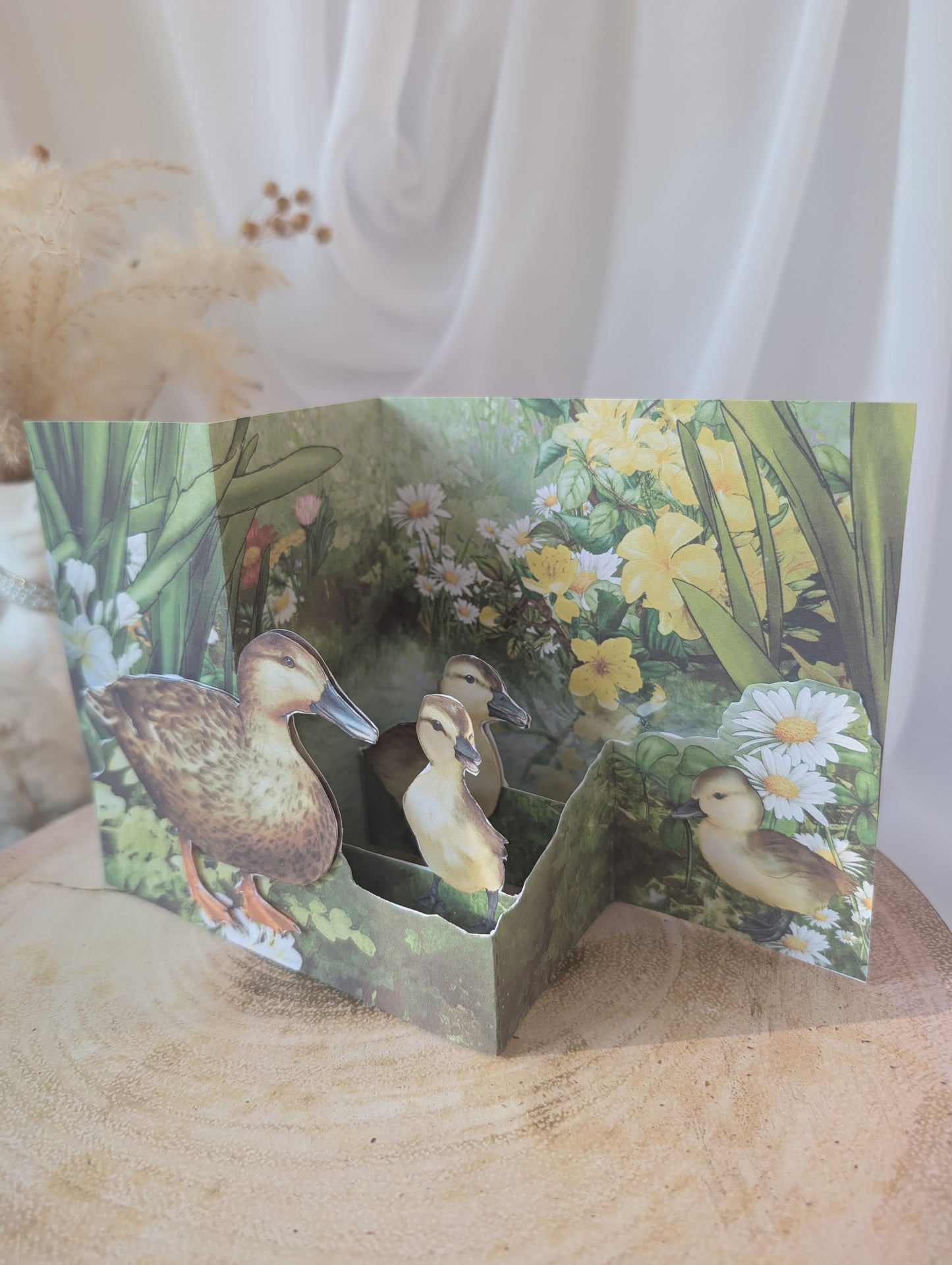 Card with a nature-themed design featuring ducks and flowers on a wooden surface.