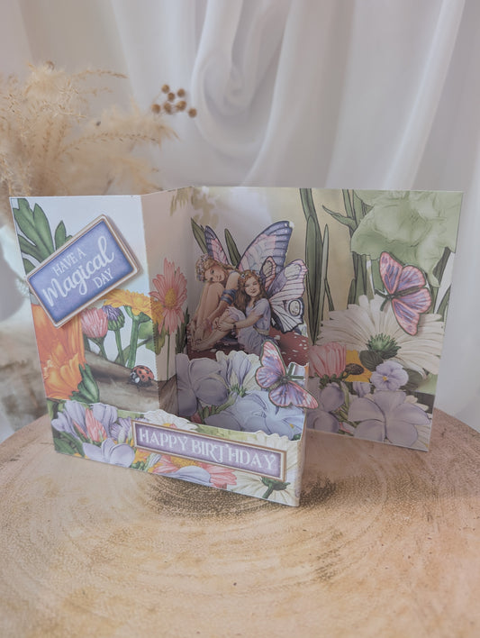 Fairy-themed birthday card with flowers and butterflies on a wooden surface.