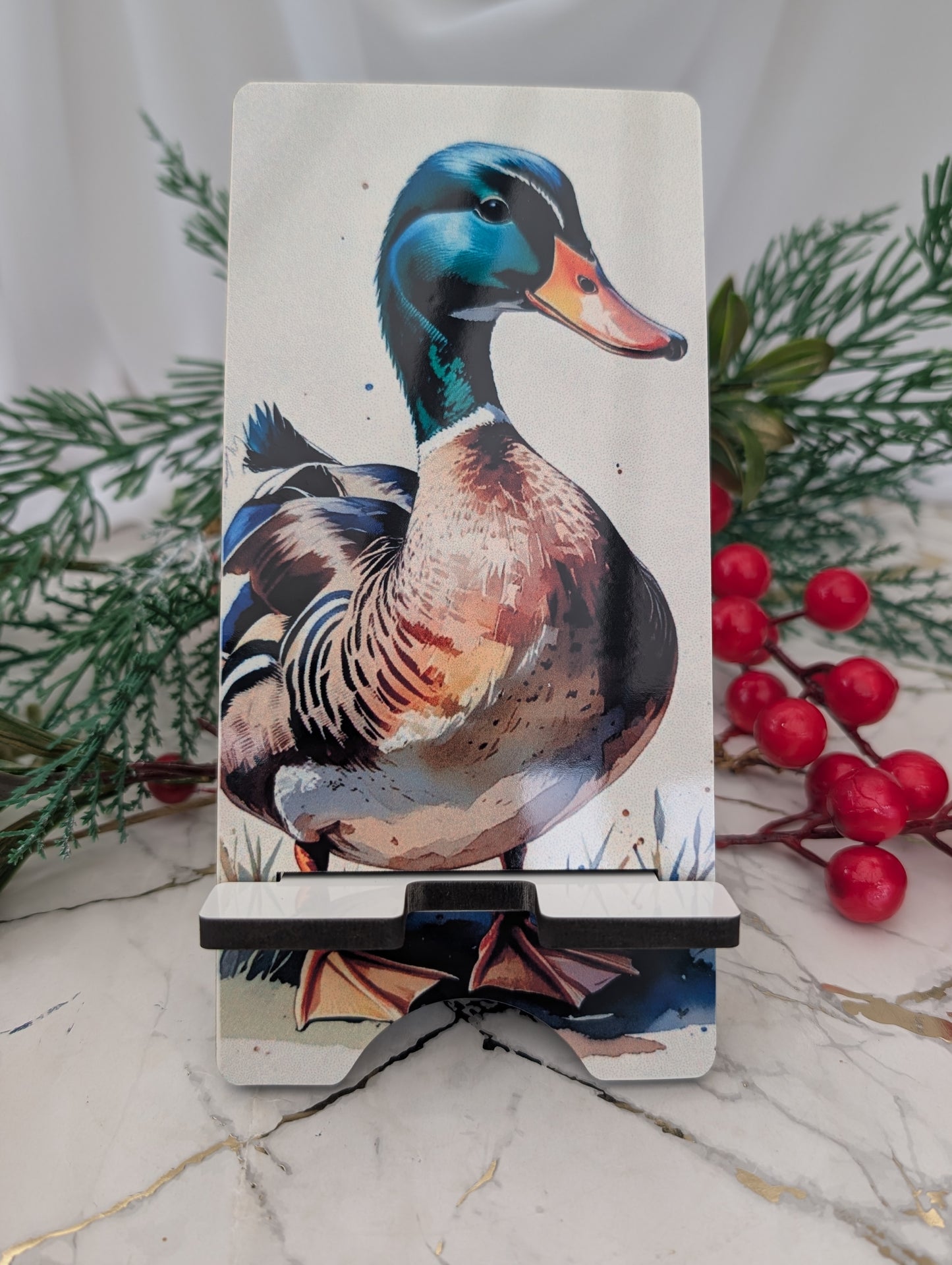 Phone stand with a duck design on a marble surface with greenery and berries.