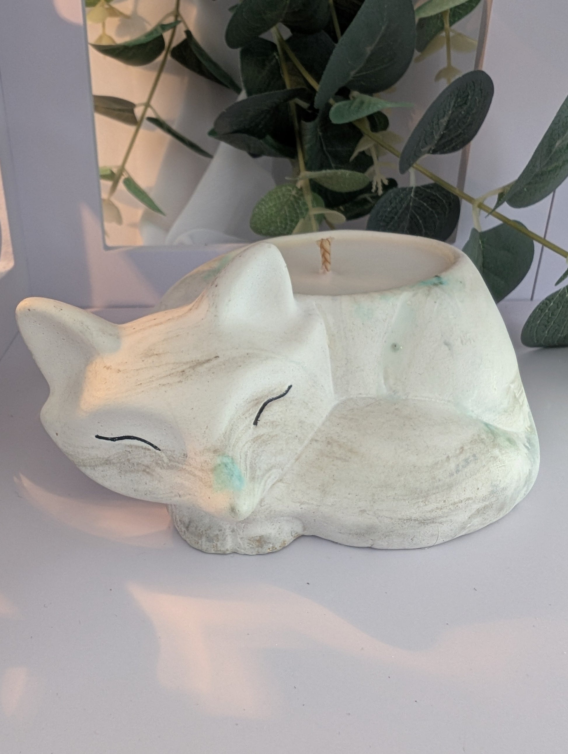 Ceramic fox ornament / fox candle  on a white surface with greenery in the background