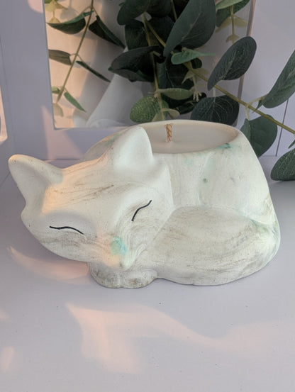 Ceramic fox ornament / fox candle  on a white surface with greenery in the background