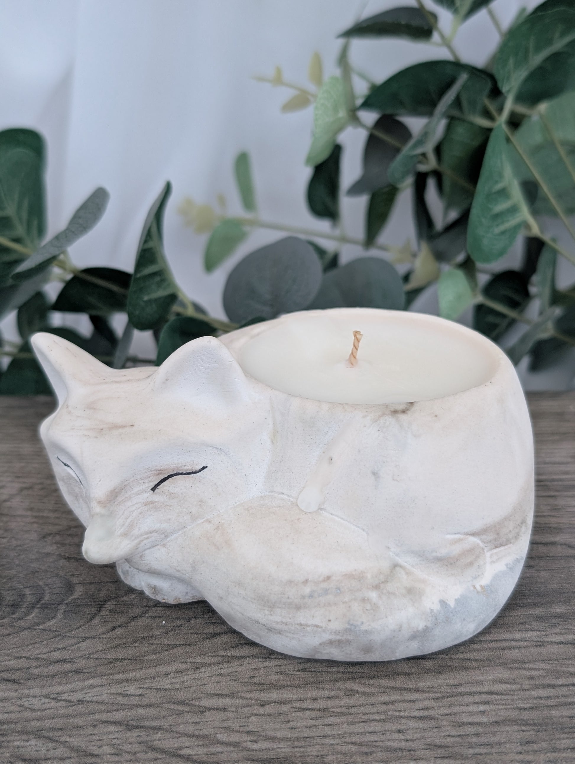 Marble-patterned fox-shaped candle holder on a wooden surface with greenery in the background