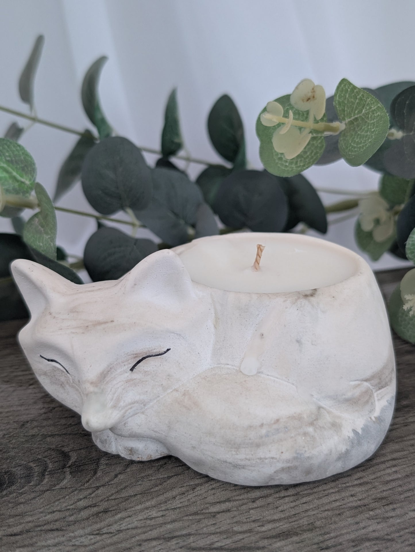 White stone fox-shaped candle holder on a wooden surface with greenery in the background