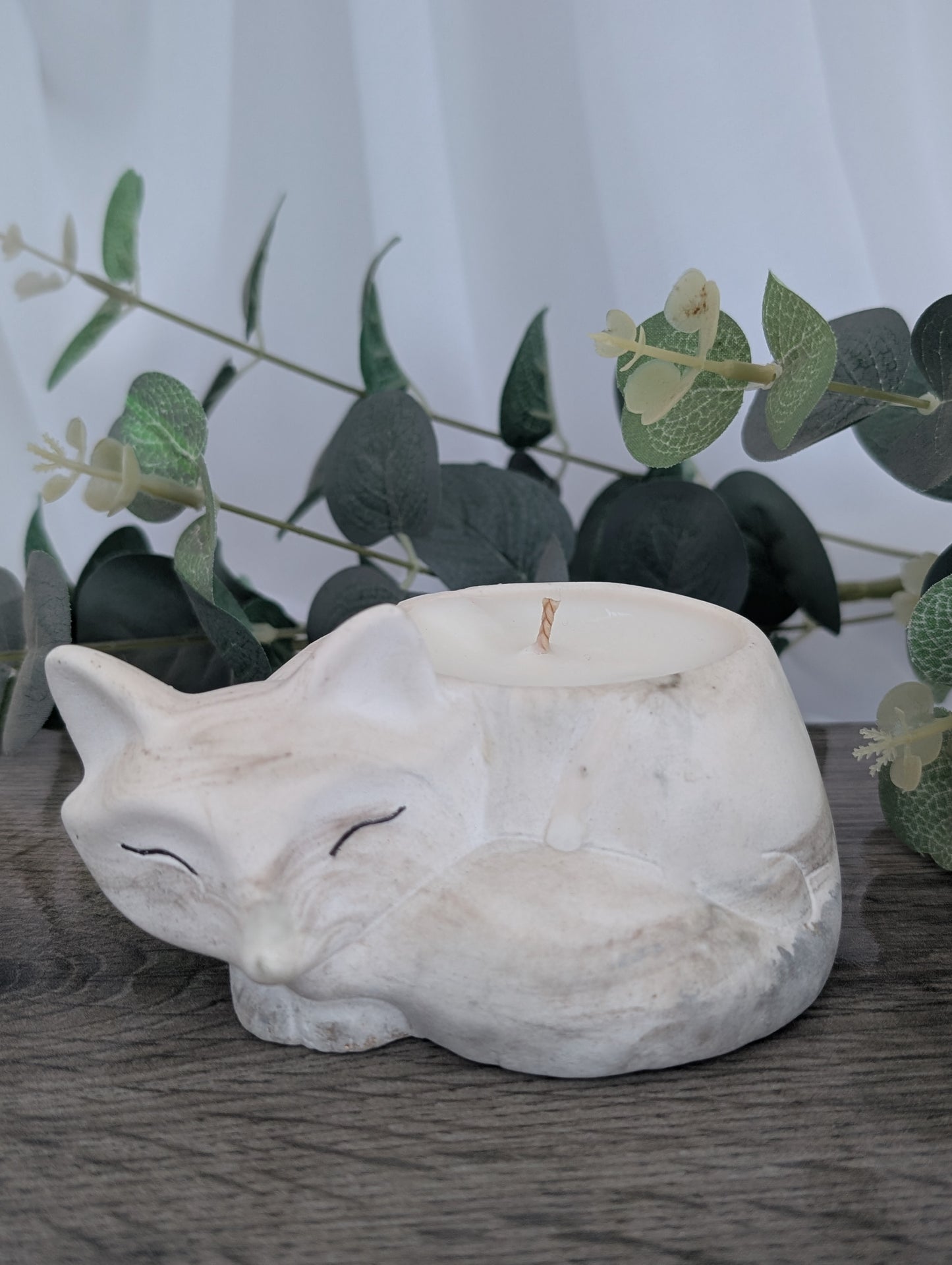 White stone fox sculpture on a wooden surface with greenery in the background