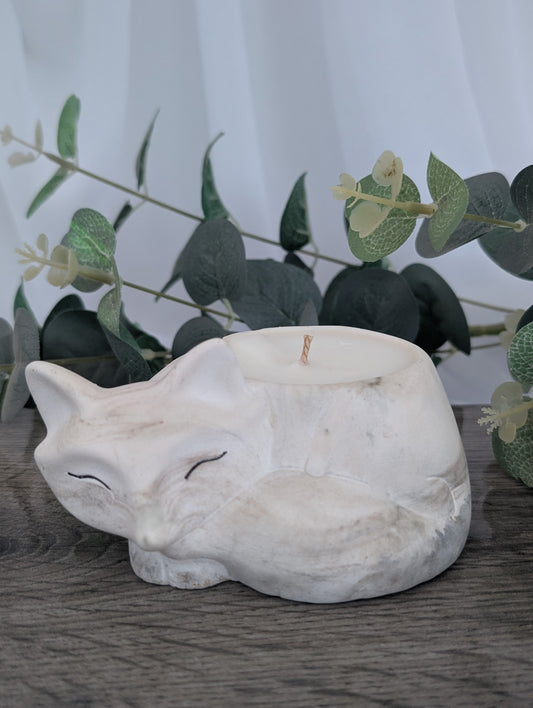 White stone fox sculpture on a wooden surface with greenery in the background