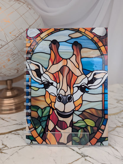 A spiral-bound notebook with a stained glass effect design featuring a giraffe's face on the cover.