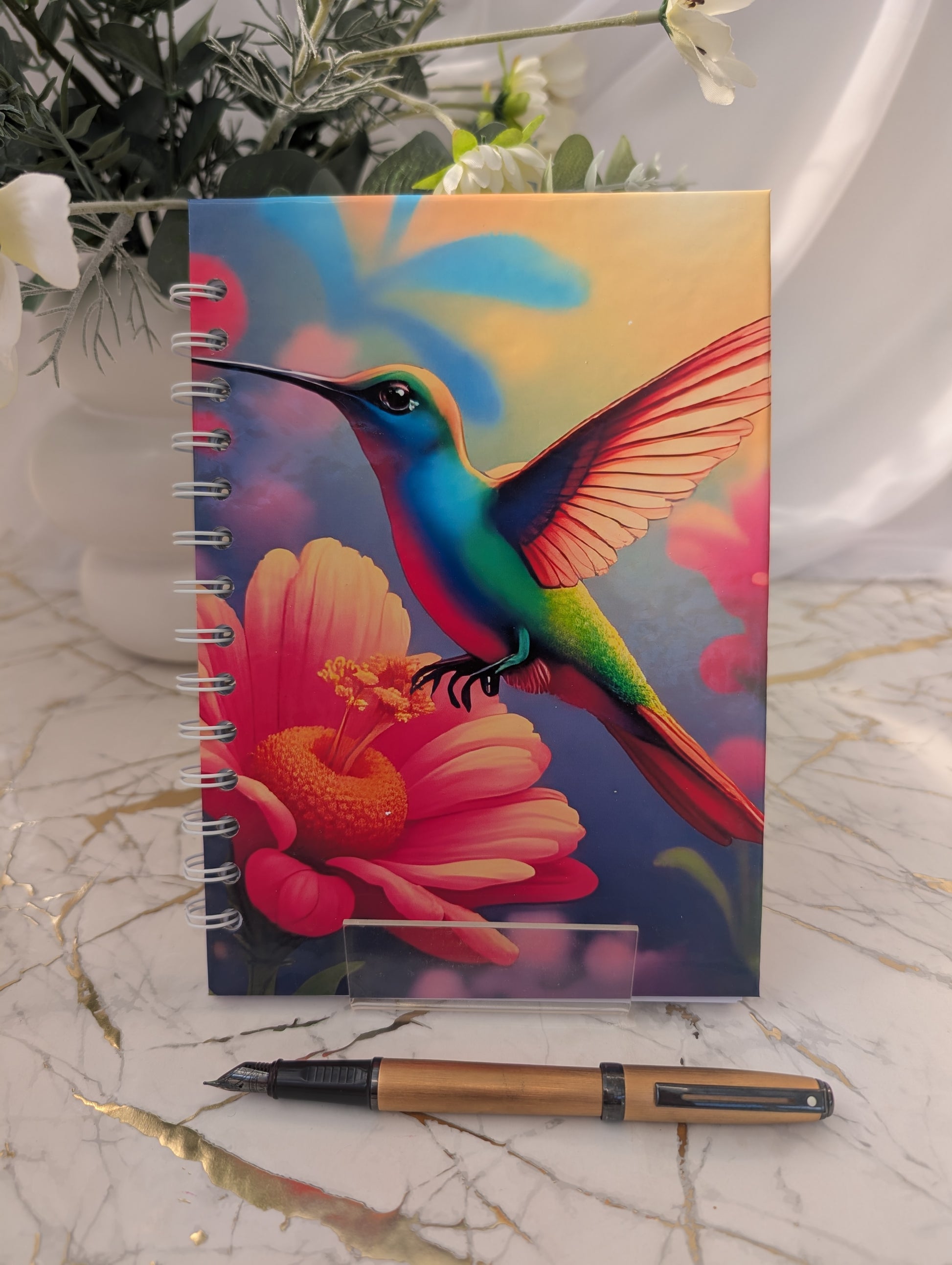 Notebook with a colorful hummingbird design on a marble surface with a pen.