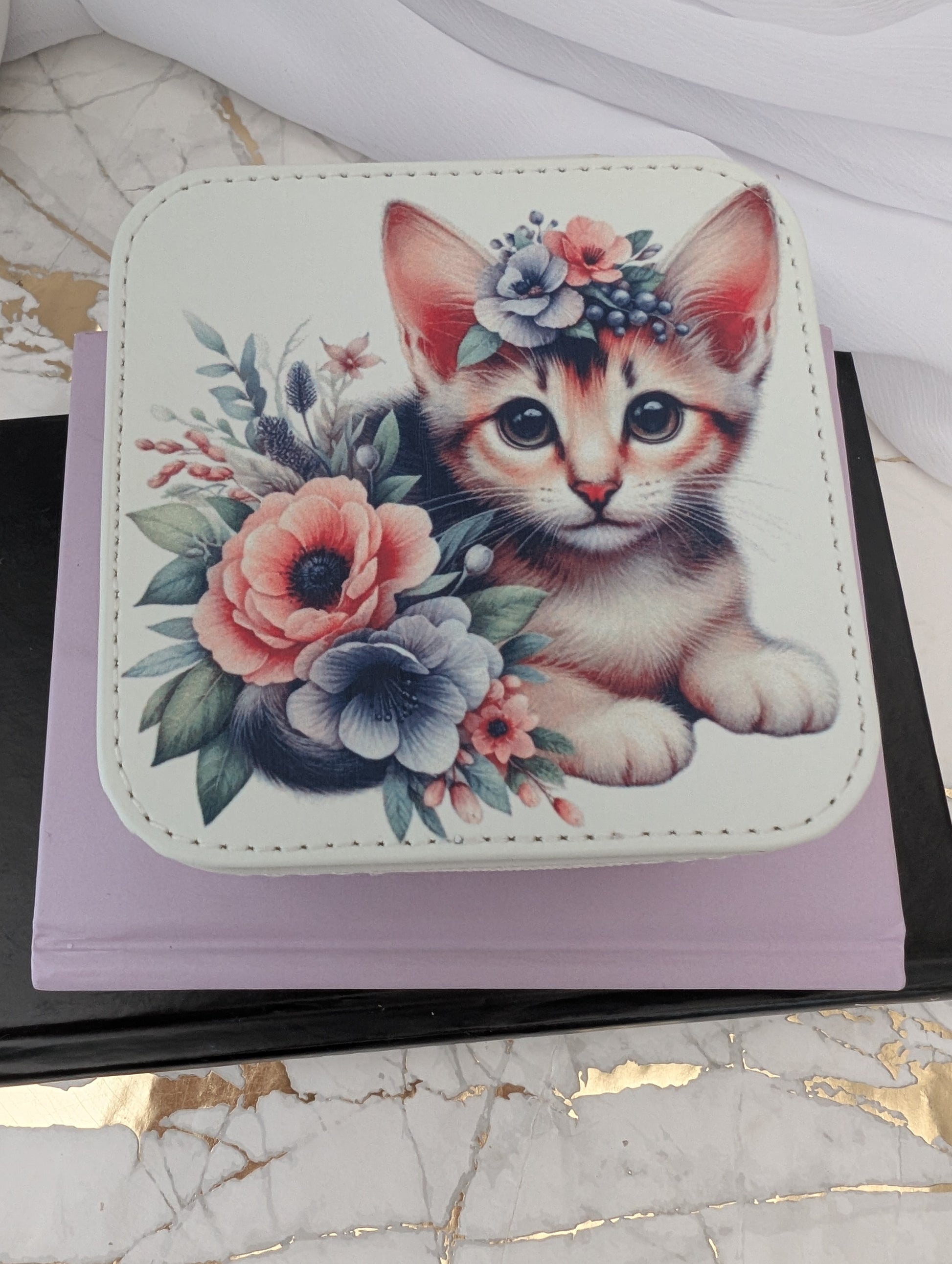 Cat Gift - Top View of cream faux leather travel jewellery box with a design of a kitten and flowers on a marble surface.
