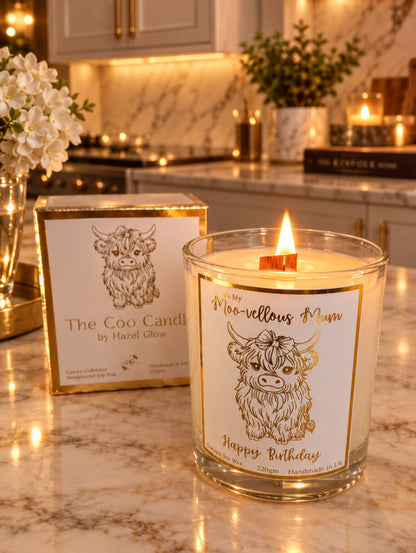 A glass jar candle labeled 'Moo-vloous Mum Happy Birthday' with a cow illustration and gold trim, shown next to its matching box packaging on a light surface.