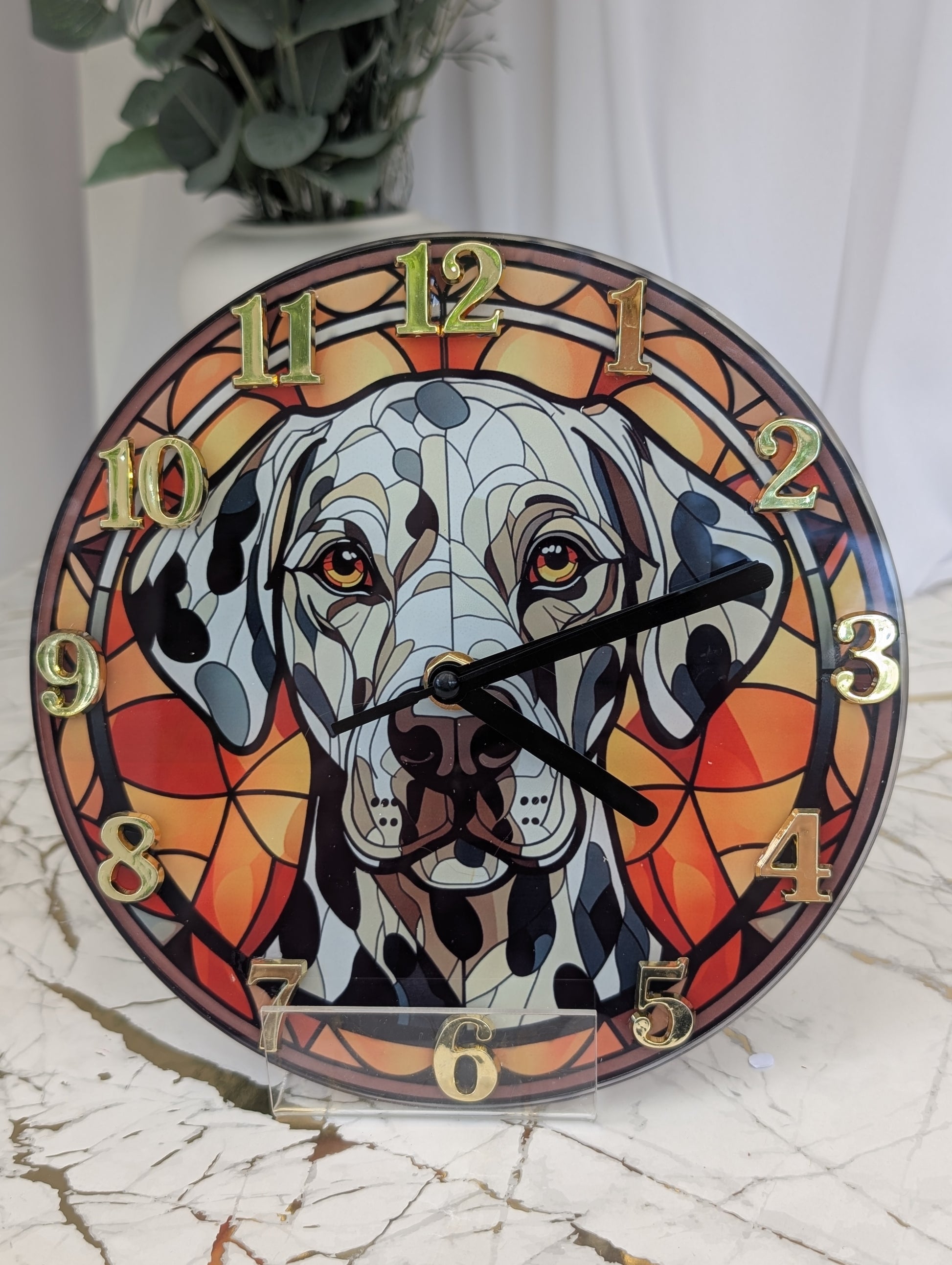 close up of Dalmation wall clock, stained glass style in red tones, with gold coloured numerals and black hands.  20cm diameter round